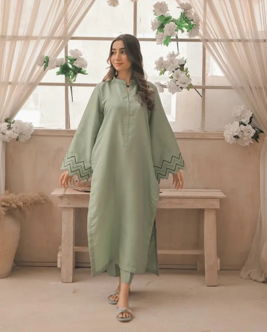 A Woman wearing an apple green dress with embroidery on sleeves and zigzag cuffs, smiling confidently. 