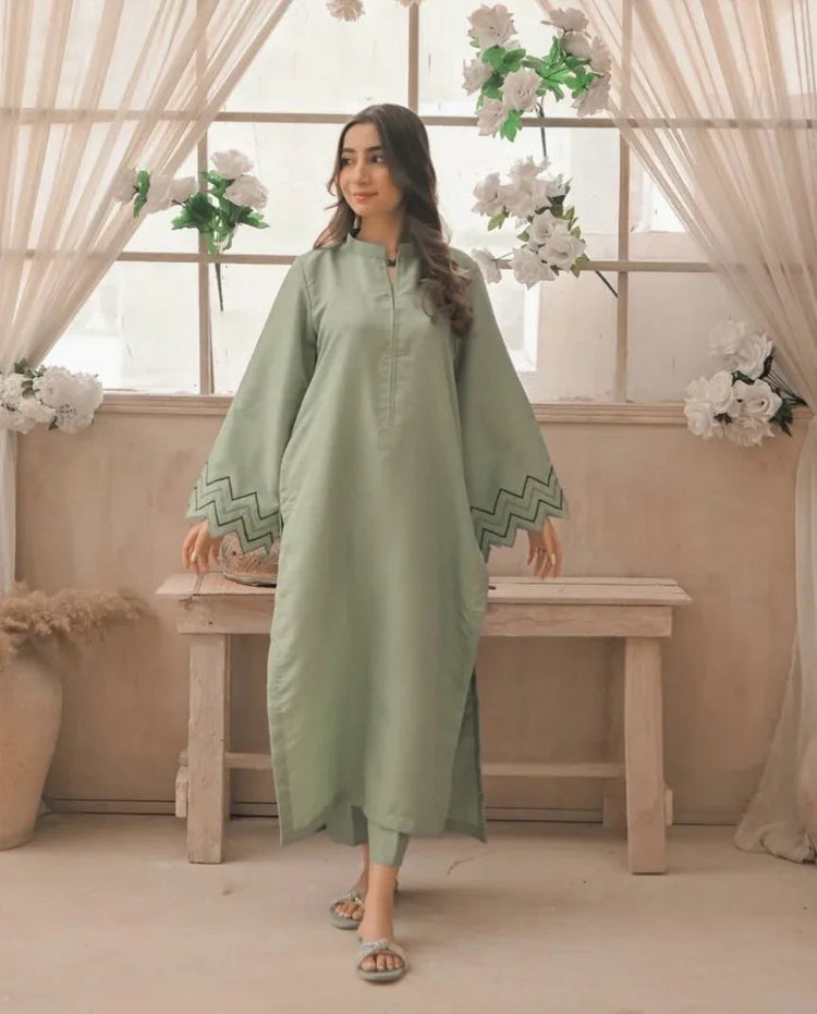 A Woman wearing an apple green dress with embroidery on sleeves and zigzag cuffs, smiling confidently. 