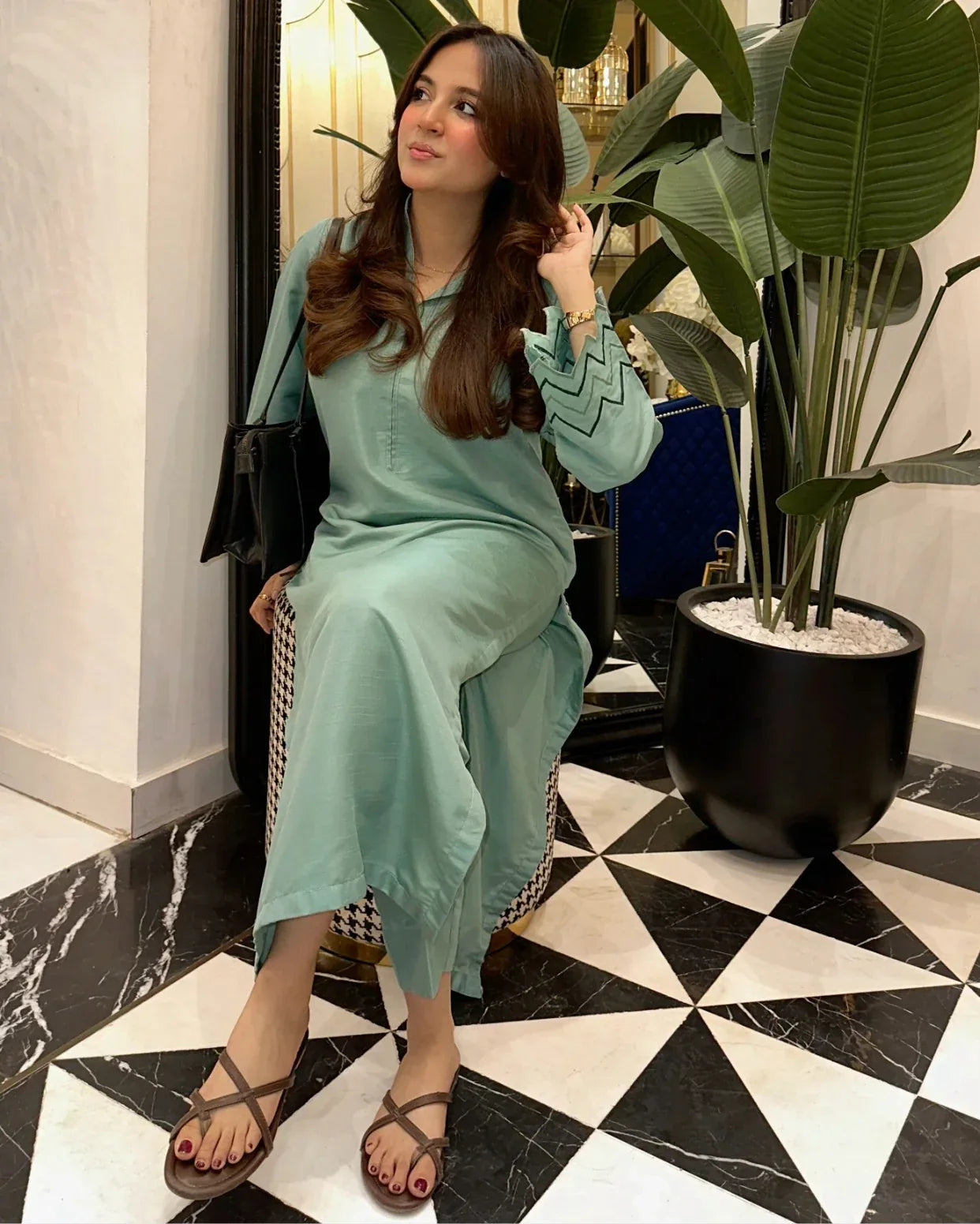 Woman in a Apple green outfit sitting on a chair indoors with plants and marble floor.