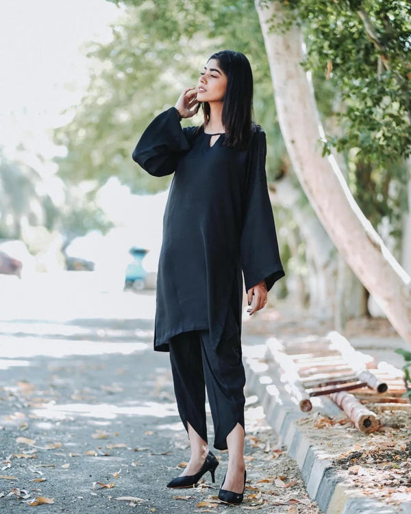 Women wearing a black outfit with leaves and trees in background.