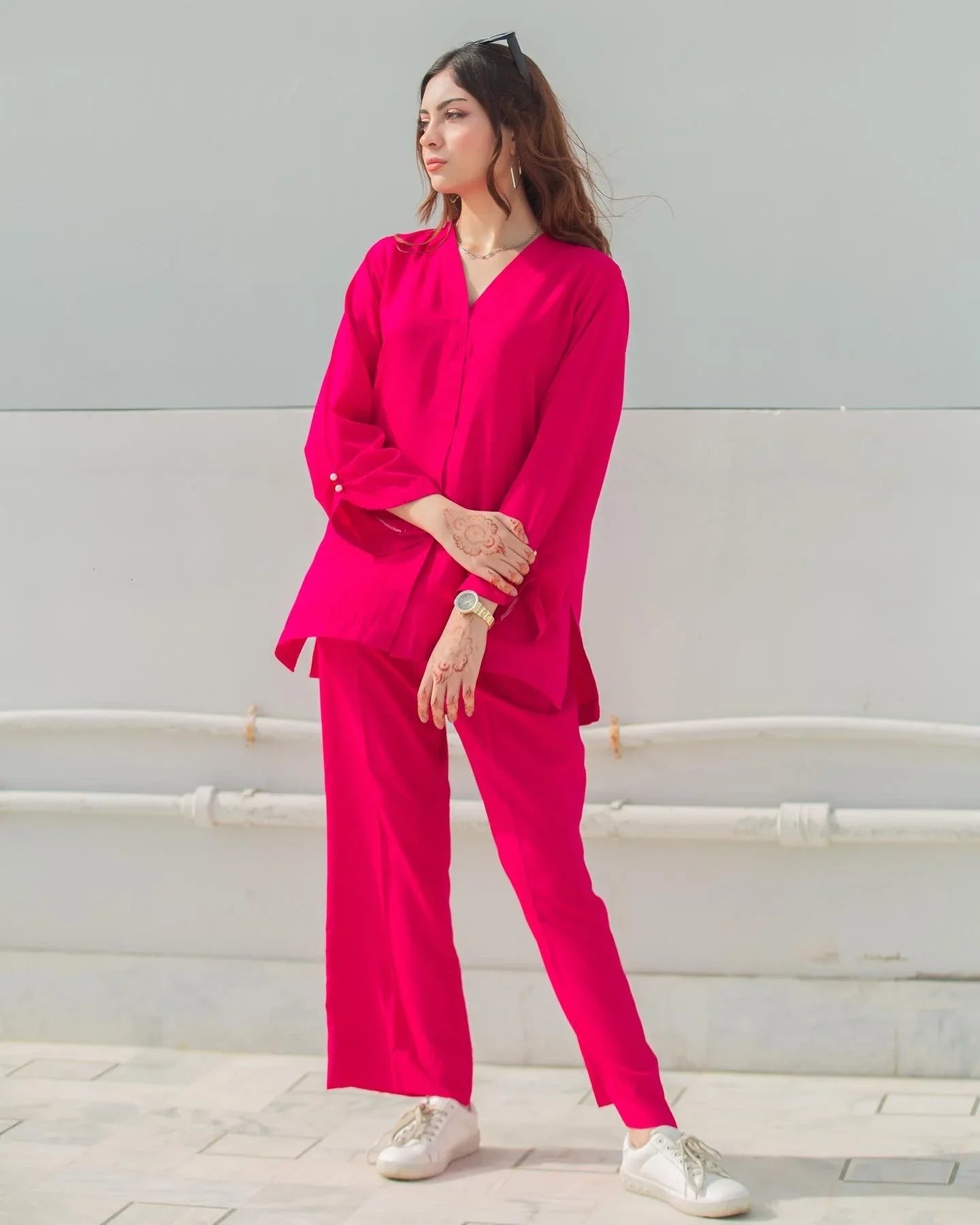 Woman wearing a bright pink outfit with white shoes against a light gray wall.