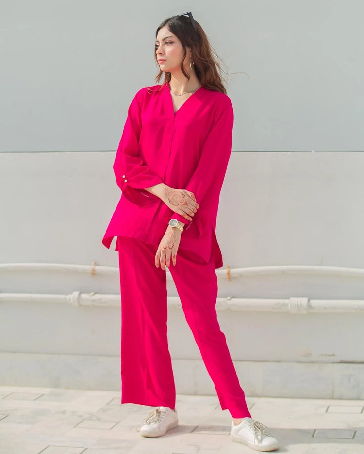 Woman wearing a bright pink outfit with white shoes against a light gray wall.