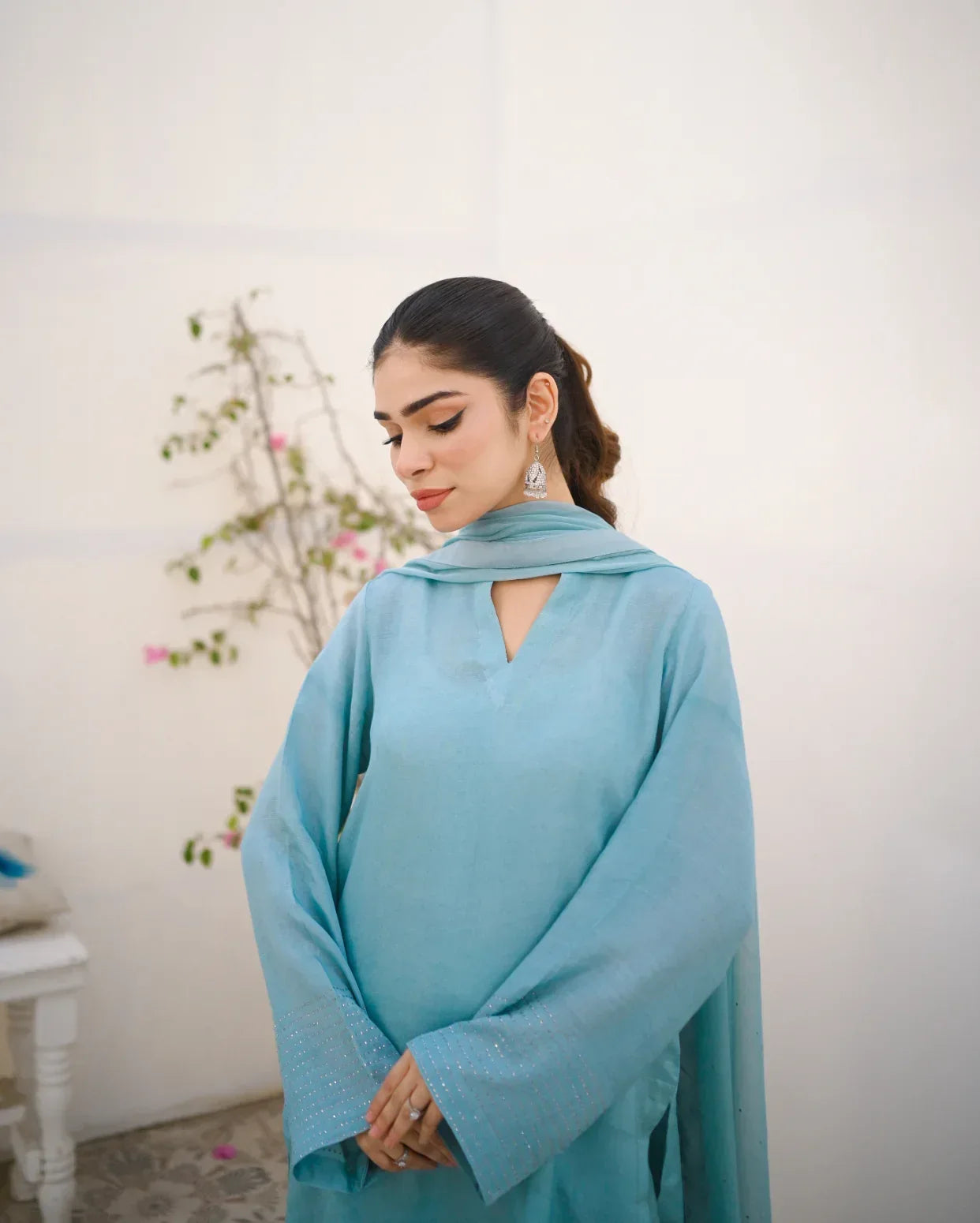 A woman wearing a Sky Blue rawsilk fabric shirt with chiffon dupatta. The dress is embellished with stone details.