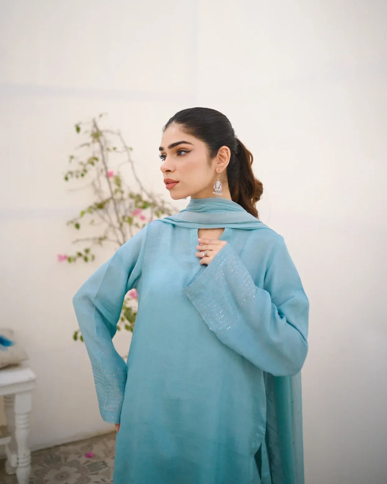 A woman wearing a Sky Blue rawsilk fabric shirt with chiffon dupatta. The dress is embellished with stone details.
