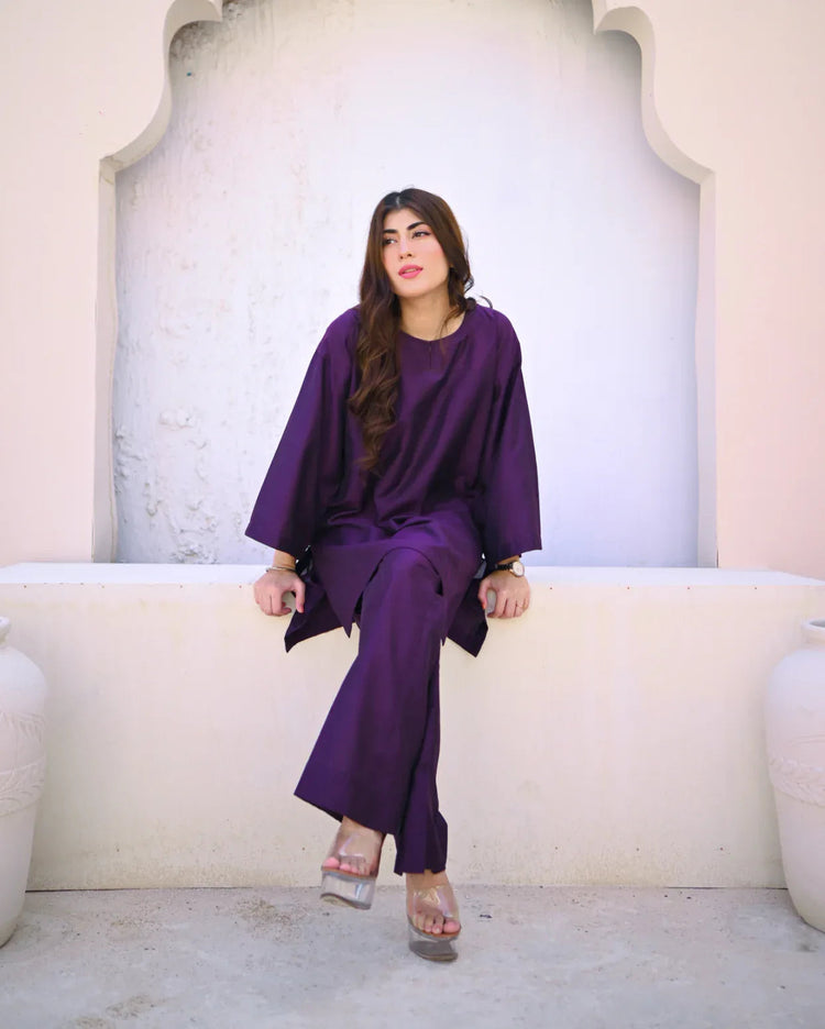 Woman in a purple outfit sitting on a white ledge with a light-colored wall behind her.