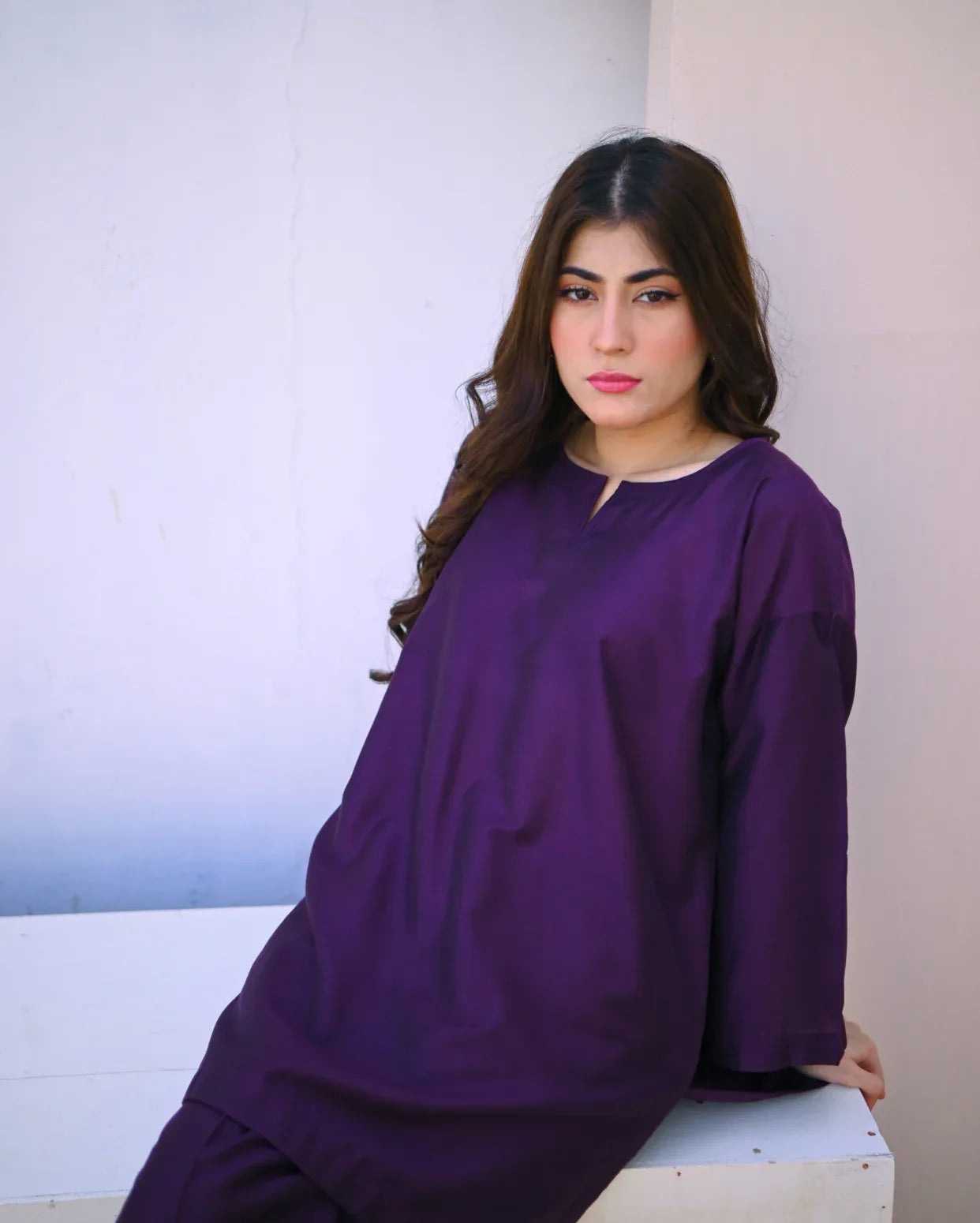 Woman wearing a purple outfit sitting on a white surface with a white wall in the background