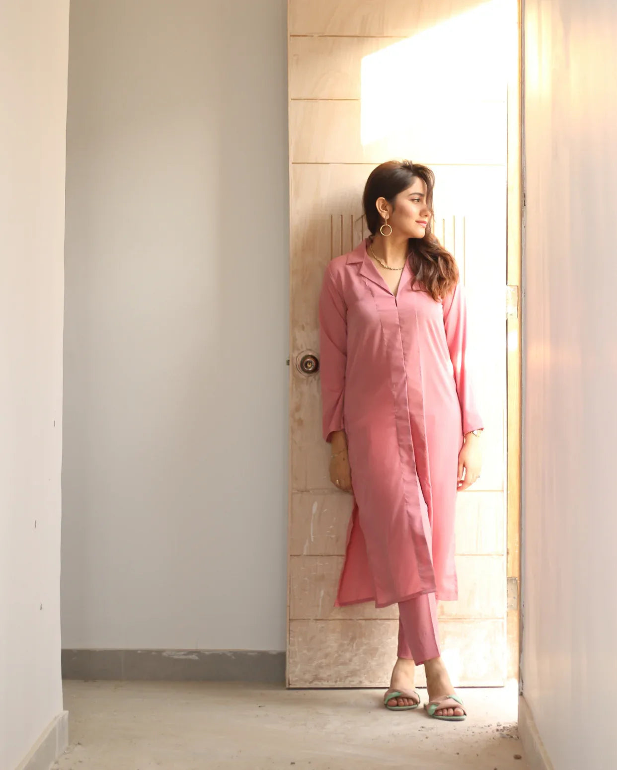 Woman in a pink outfit standing in a well-lit room with a neutral background.