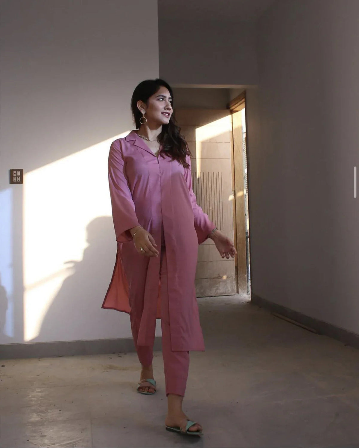 Woman in a pink outfit walking in a well-lit room with a neutral background.