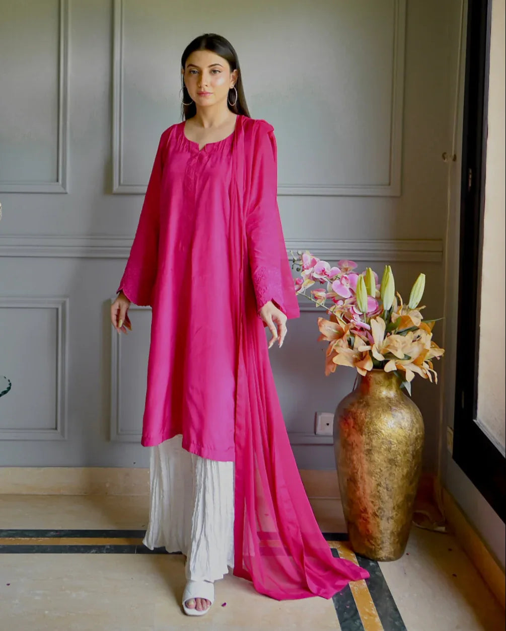 Women wearing a three piece pink color dress which includes a shirt with embroidery on sleeves, dhaka lehenga and a chiffon dupatta.