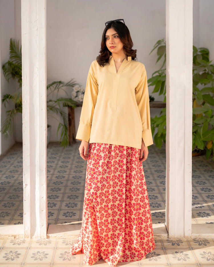Woman wearing a lemon yellow top and red floral skirt standing in a room with plants.