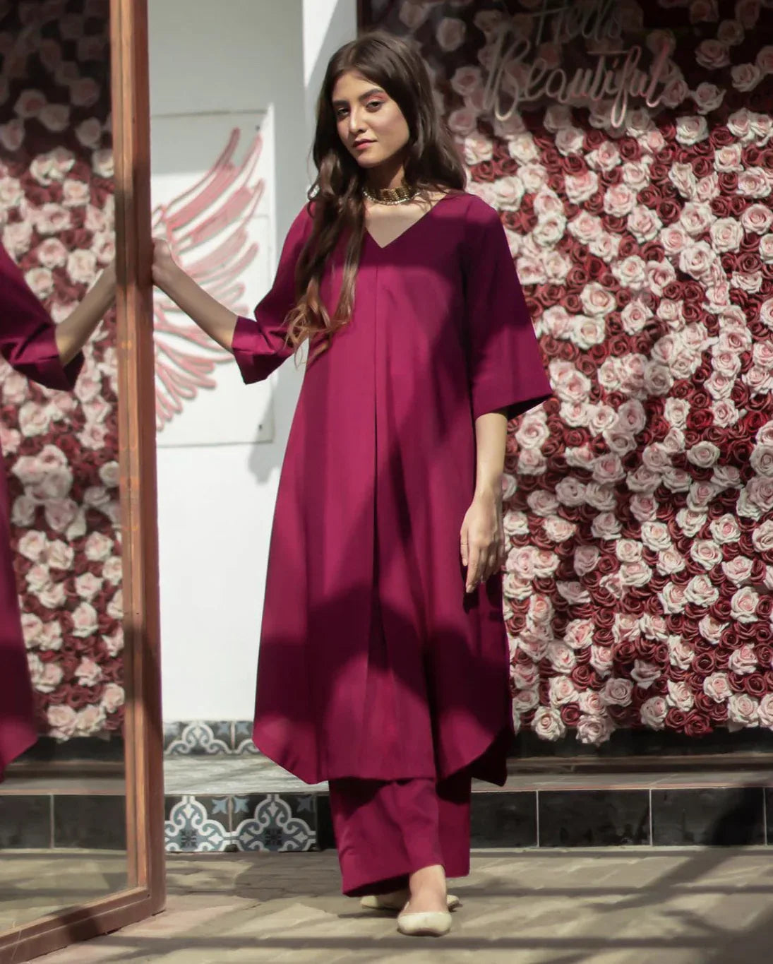 A woman in a stitched magenta color dress standing confidently, showcasing her stylish outfit.