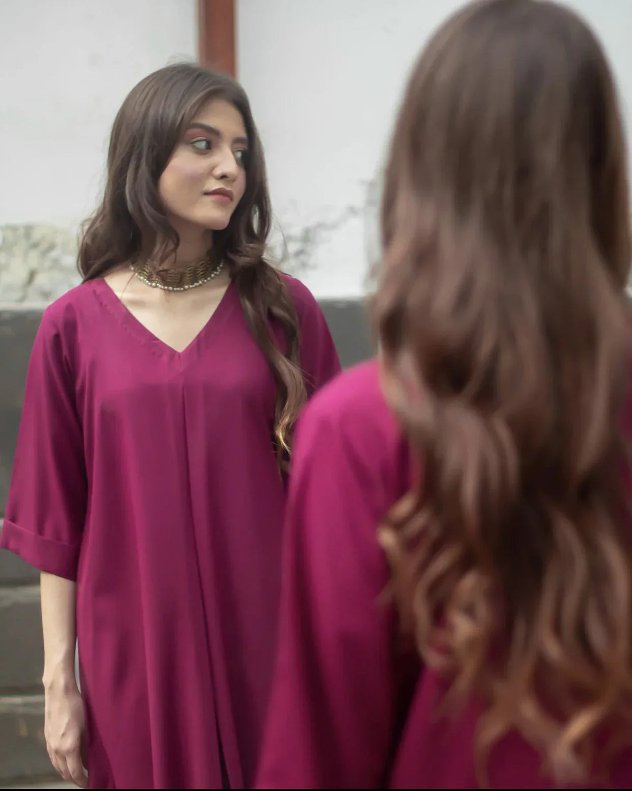 A woman in a magenta color dress standing confidently, showcasing her stylish outfit.