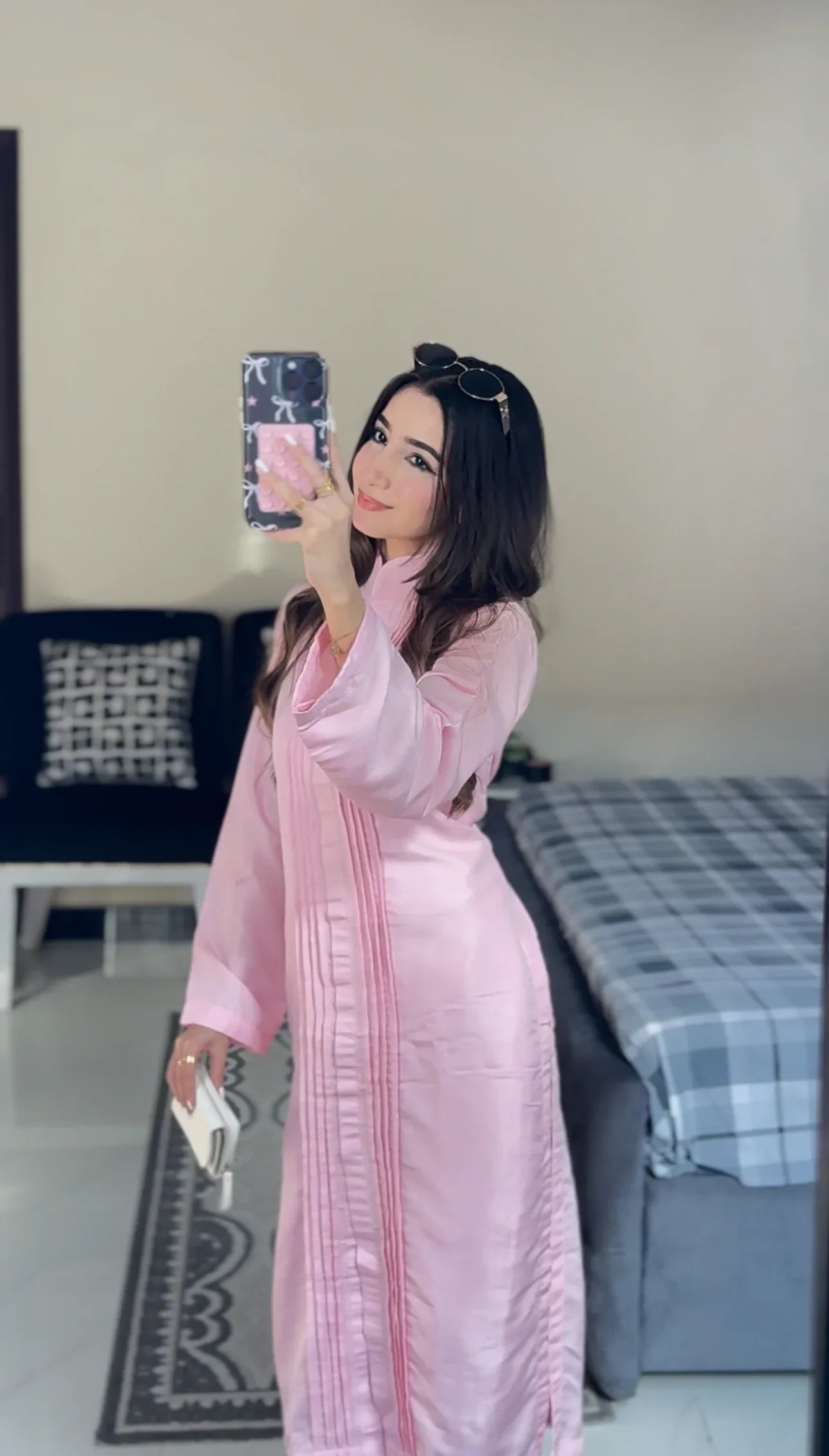 Woman in a pink dress taking a mirror selfie in a room with a bed and chair.