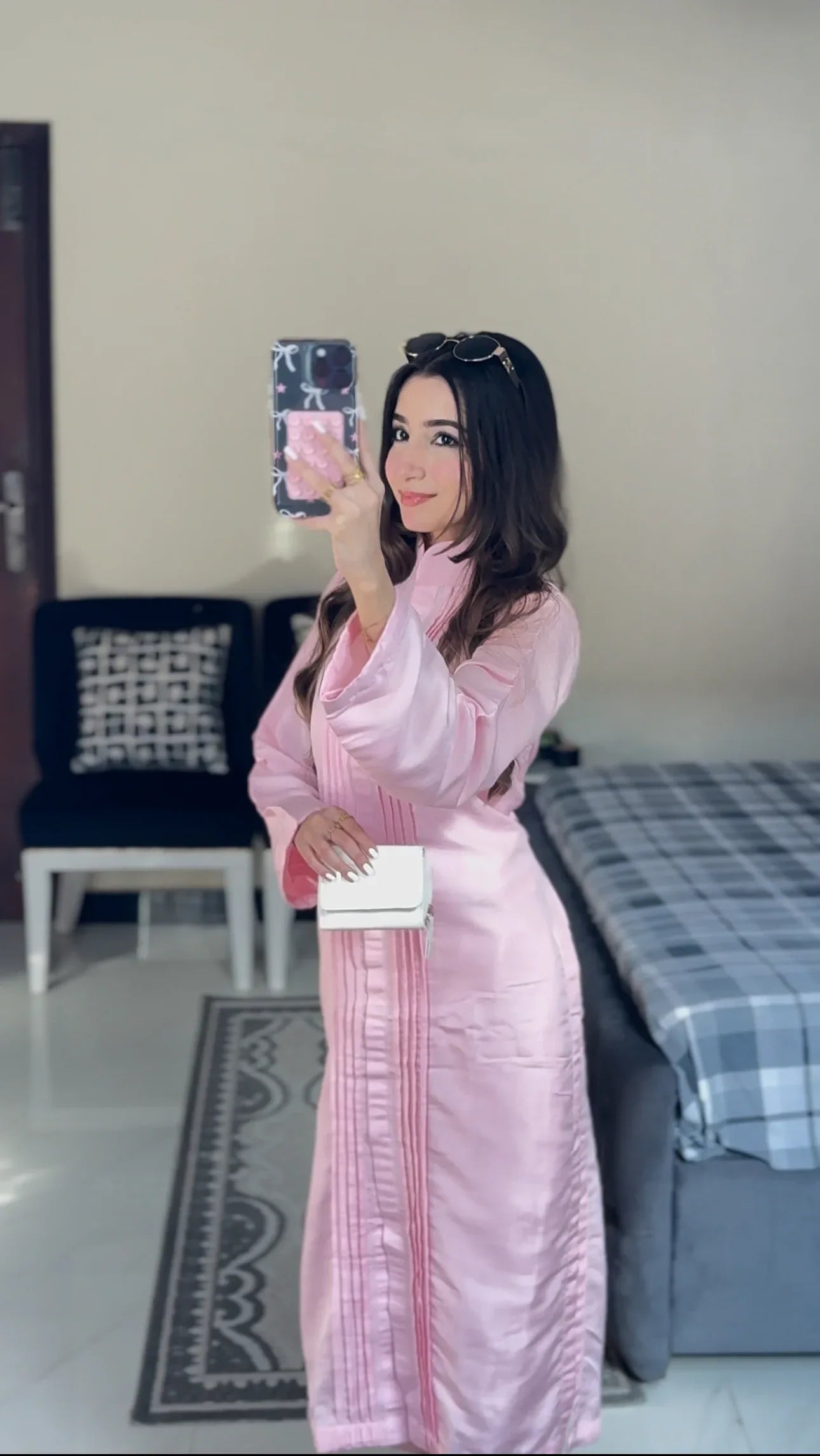 Woman in a pink dress taking a mirror selfie in a room with a bed and chair.