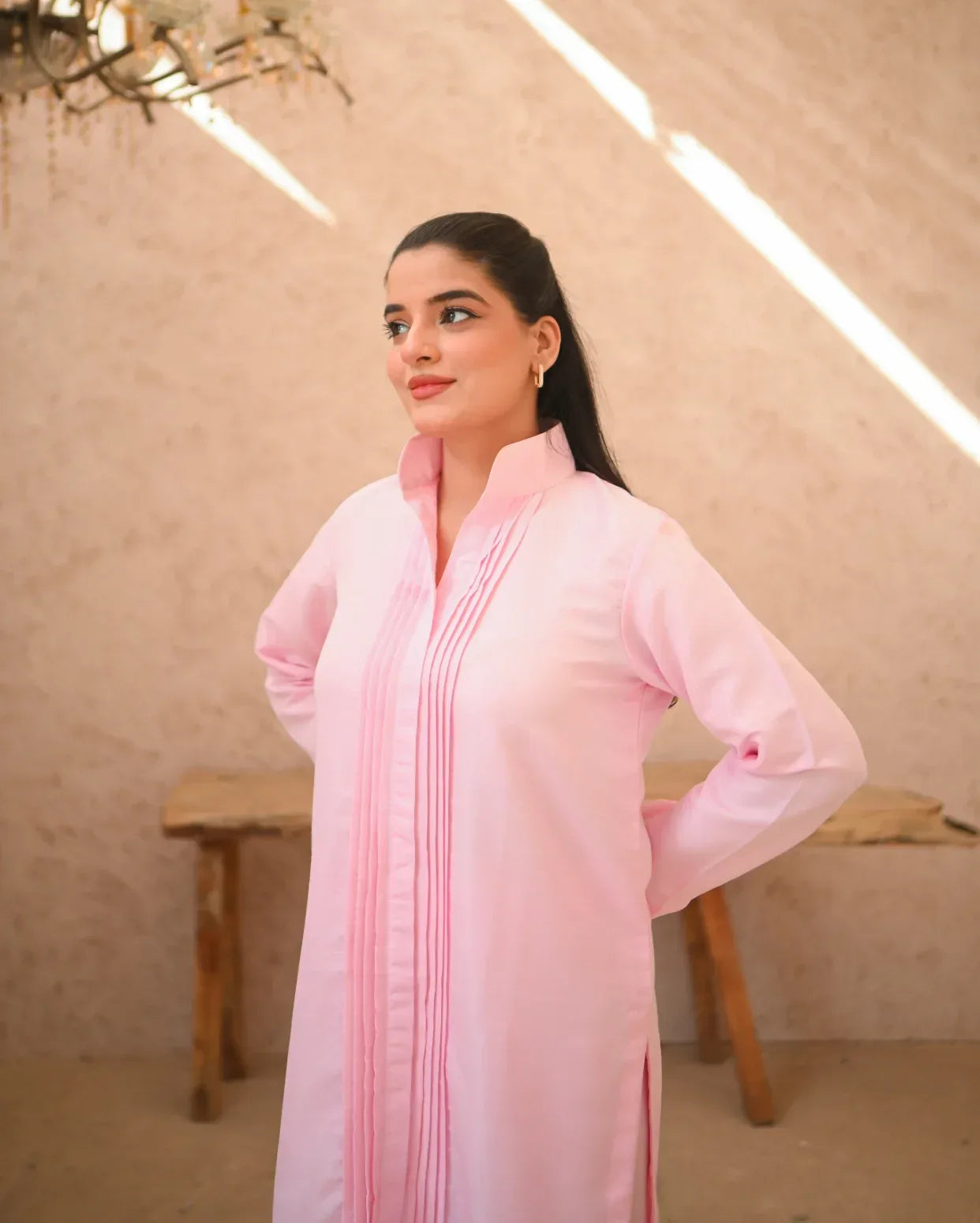 A woman standing in a sunny area wearing a pink two-piece rawsilk dress with long sleeves and pink stripes.
