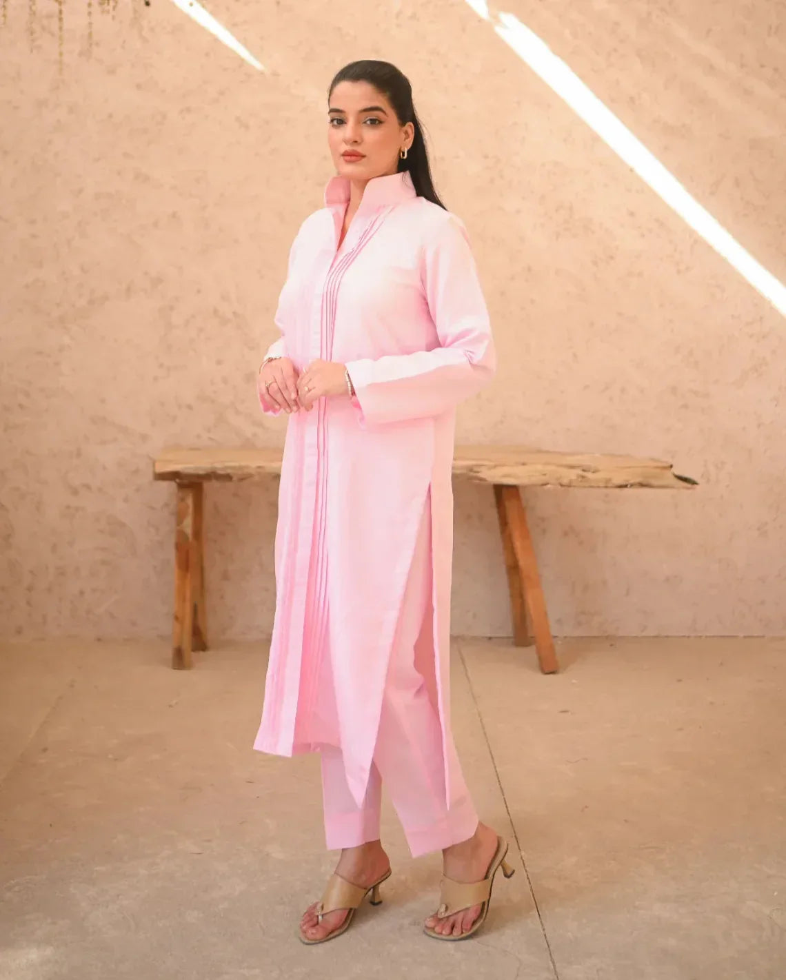 A woman standing in a sunny area wearing a pink two-piece rawsilk dress with long sleeves and pink stripes paired with a culotte.
