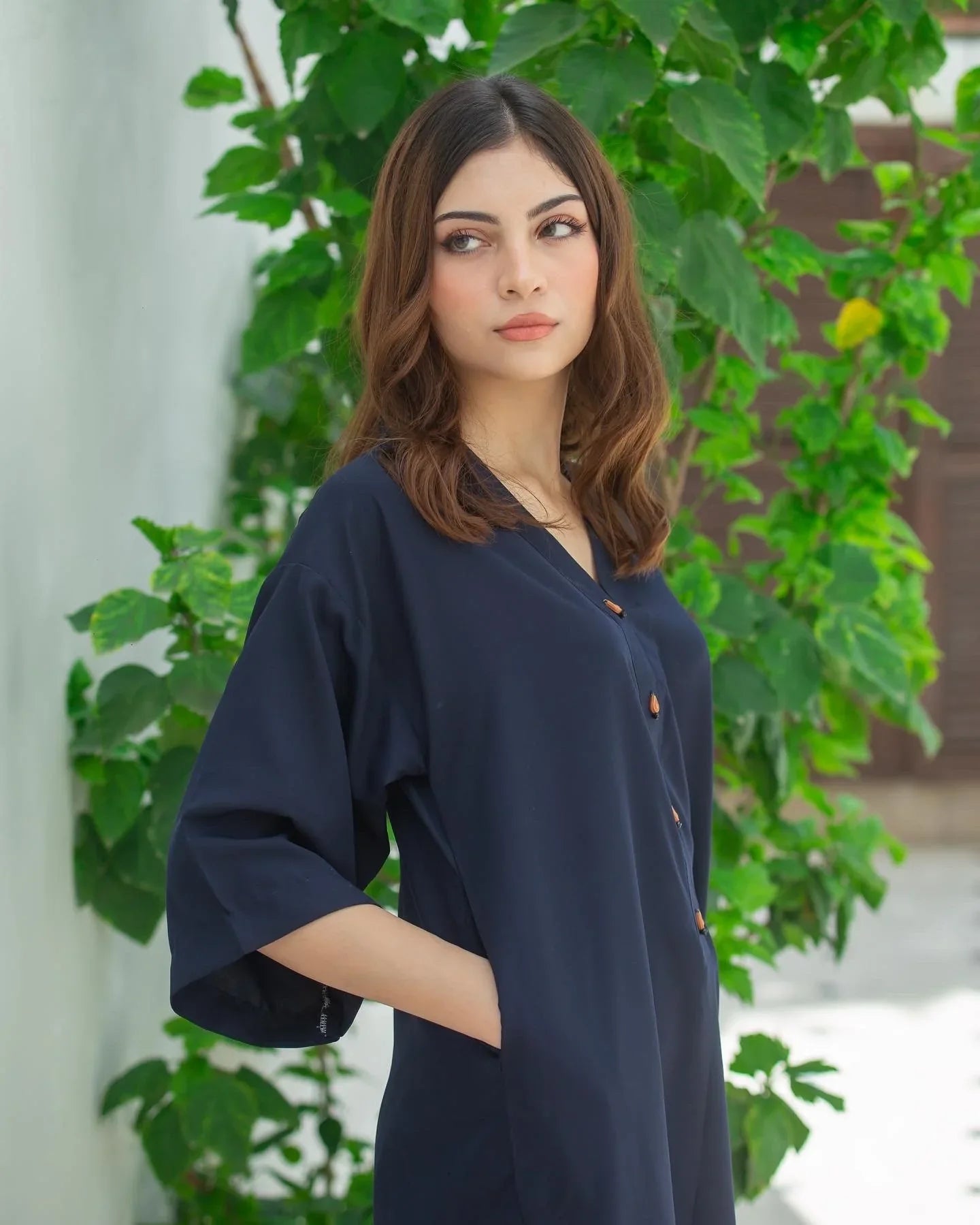 Women wearing a navy blue dress with plants in the background.