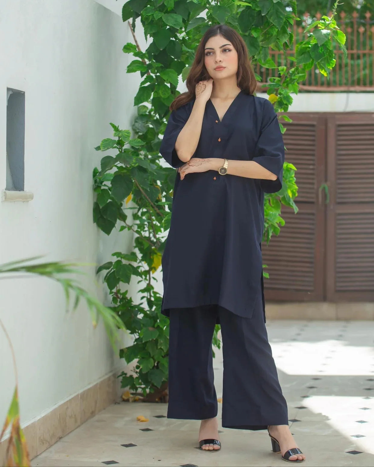 Woman in a navy blue outfit standing outdoors with greenery in the background