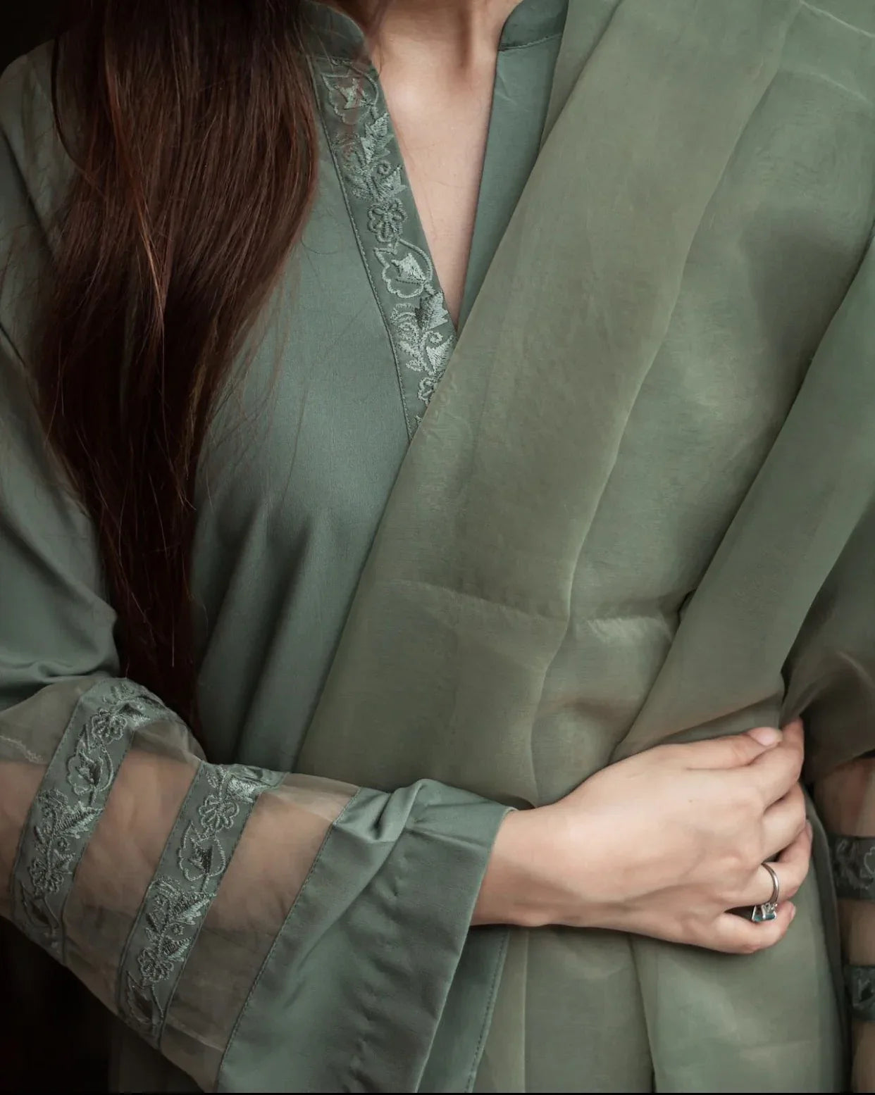 Close up on the details of embroidery on sleeves and neck line of olive green dress.
