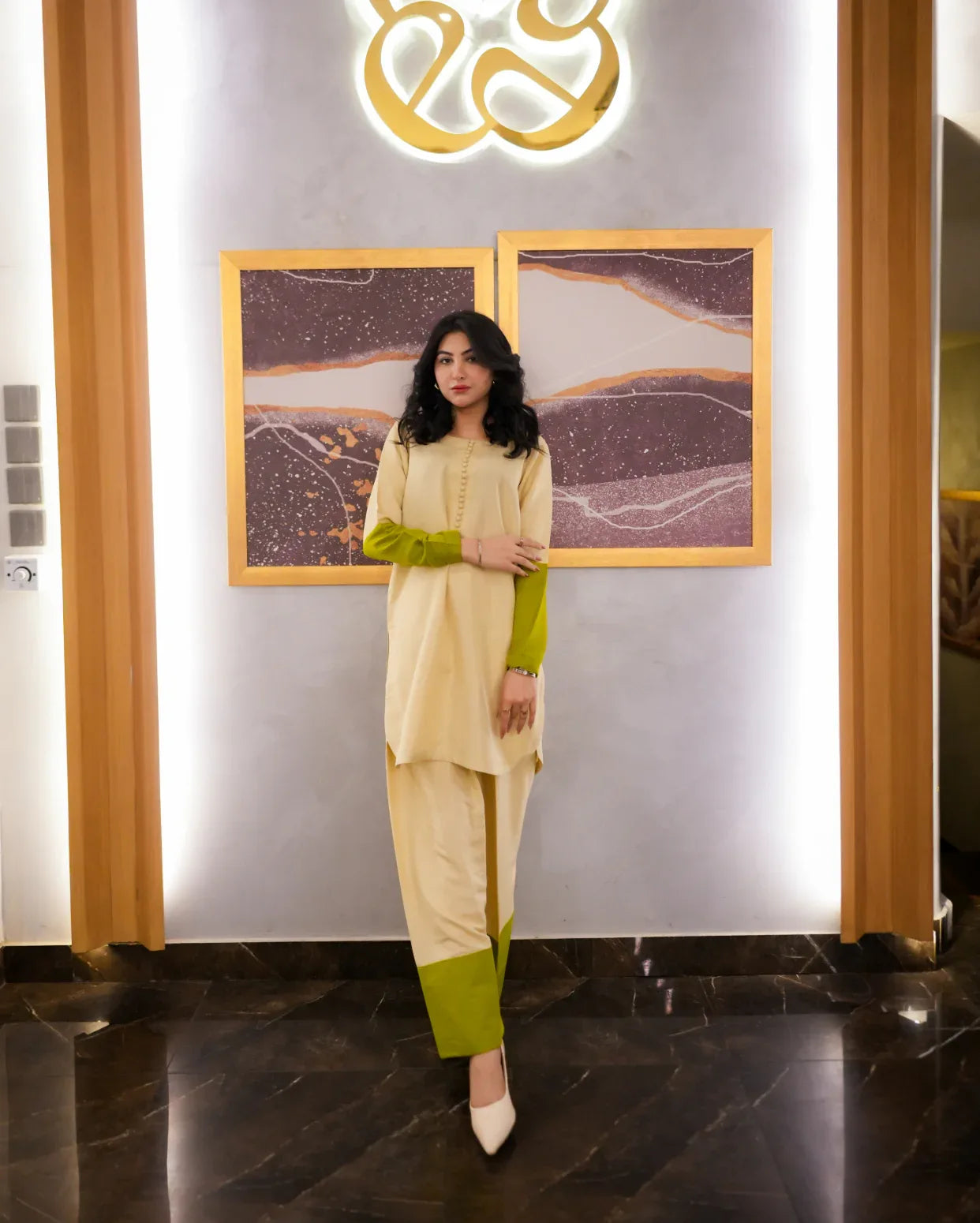 Woman in a beige and green outfit standing in front of a decorative wall with gold accents.