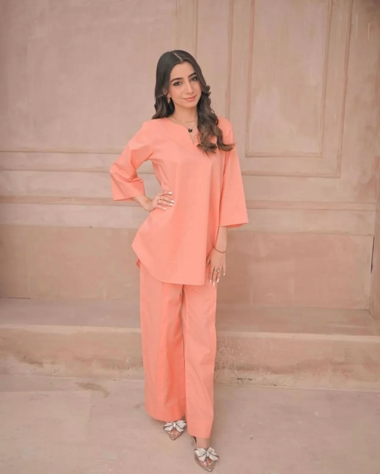 Woman wearing a peach outfit against a beige wall.