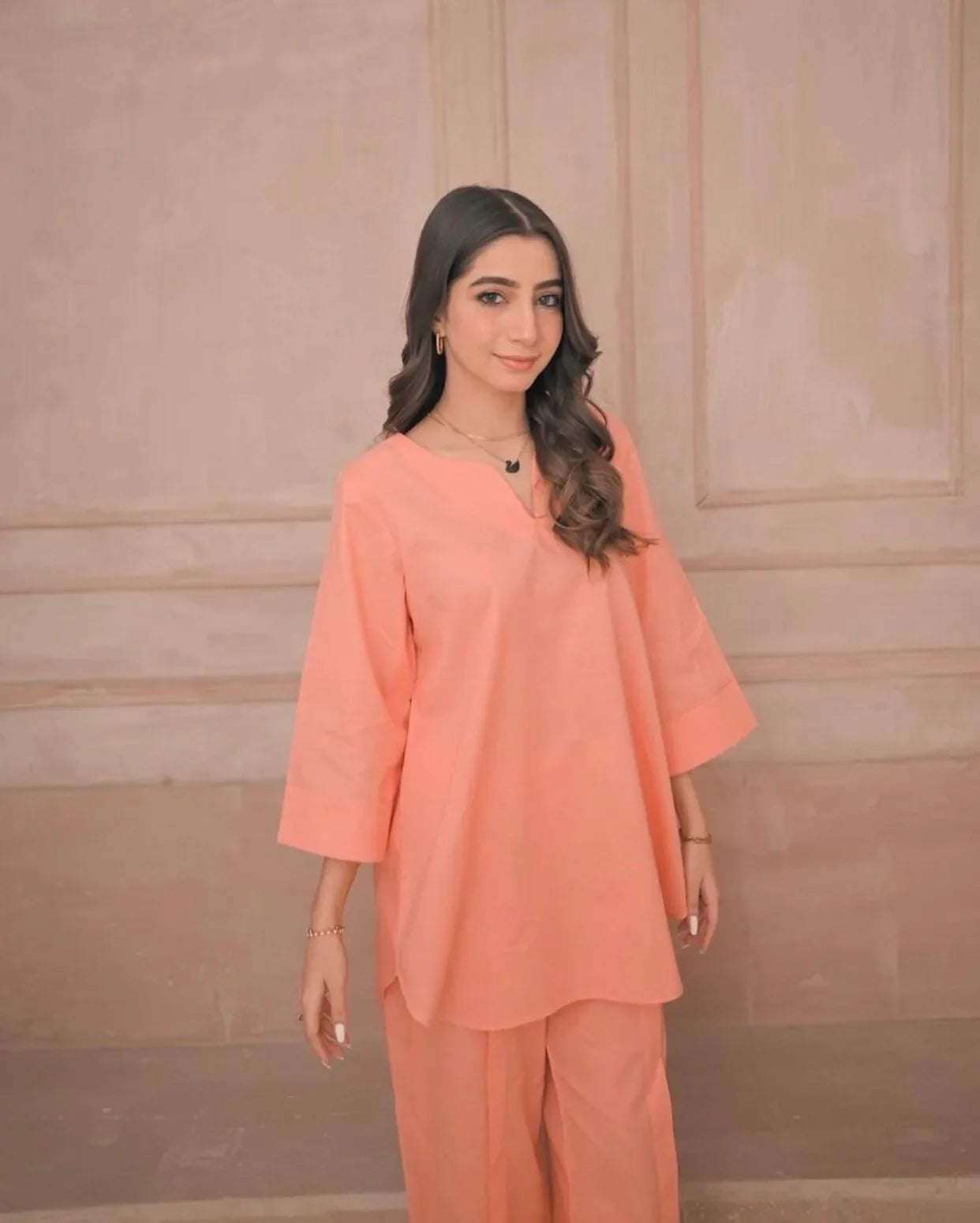 Woman wearing a peach outfit against a beige wall