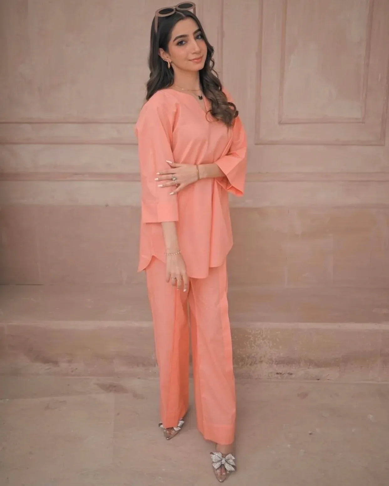 Woman wearing a peach outfit standing against a beige wall.