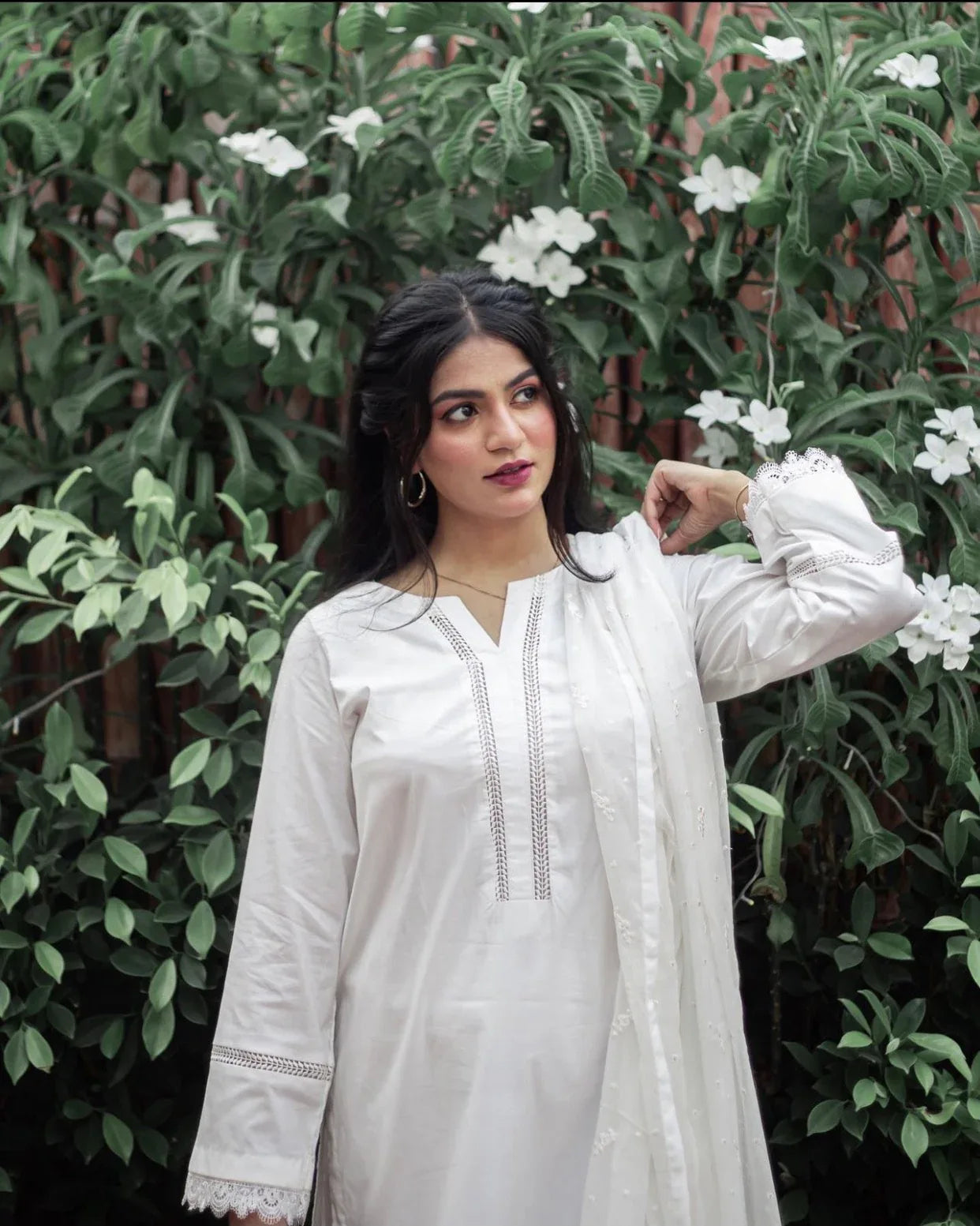A woman in white three piece dress outdoor on a sunny day, surrounded by greenery.
