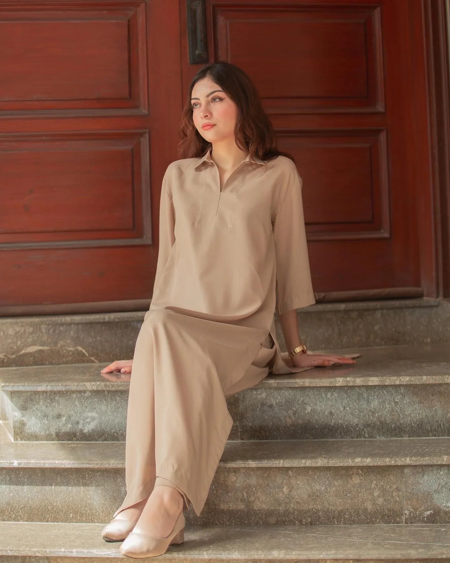 A woman in a Phone Dress sitting in front of large wooden doors with a thoughtful expression. 