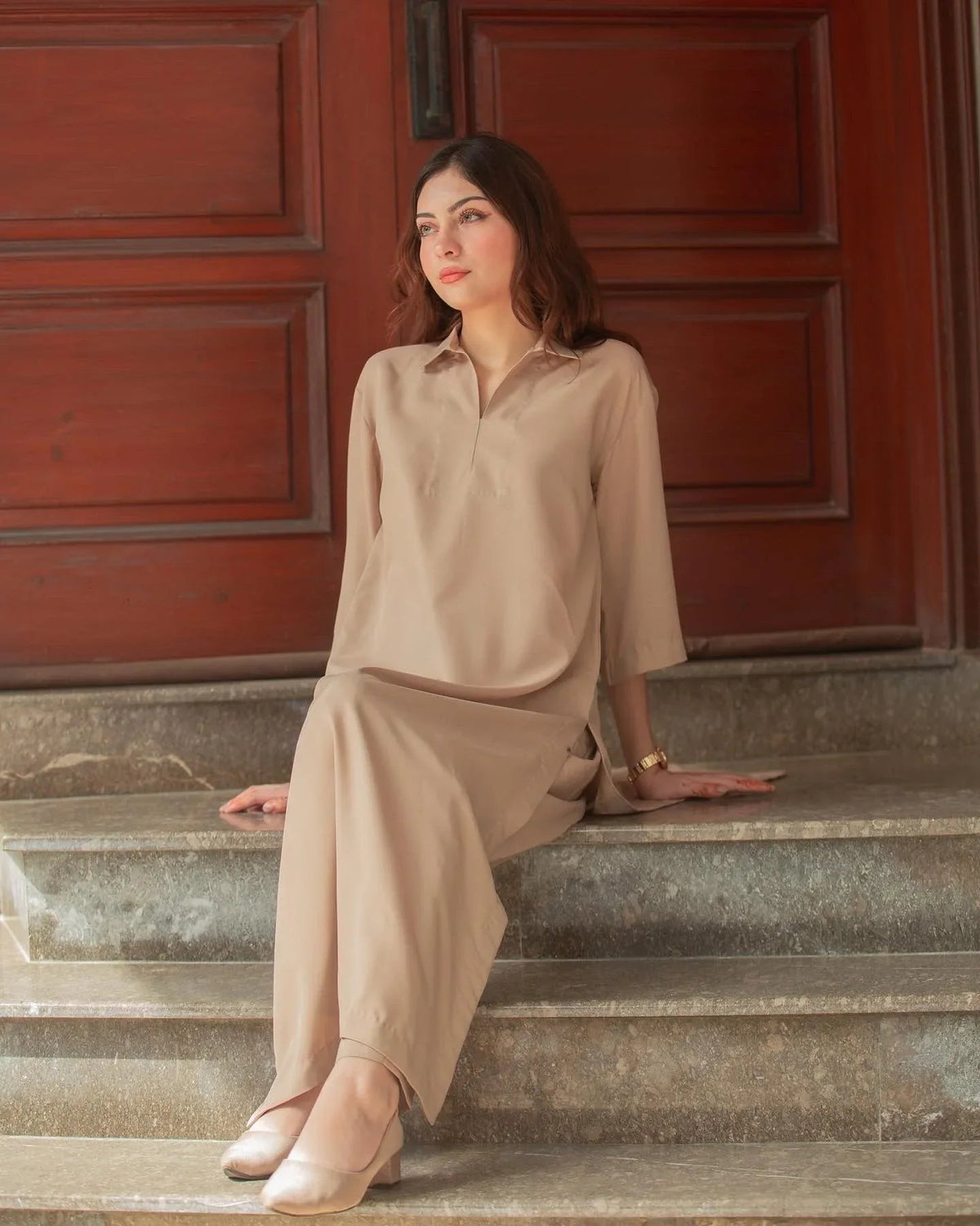 A woman in a Phone Dress sitting in front of large wooden doors with a thoughtful expression. 