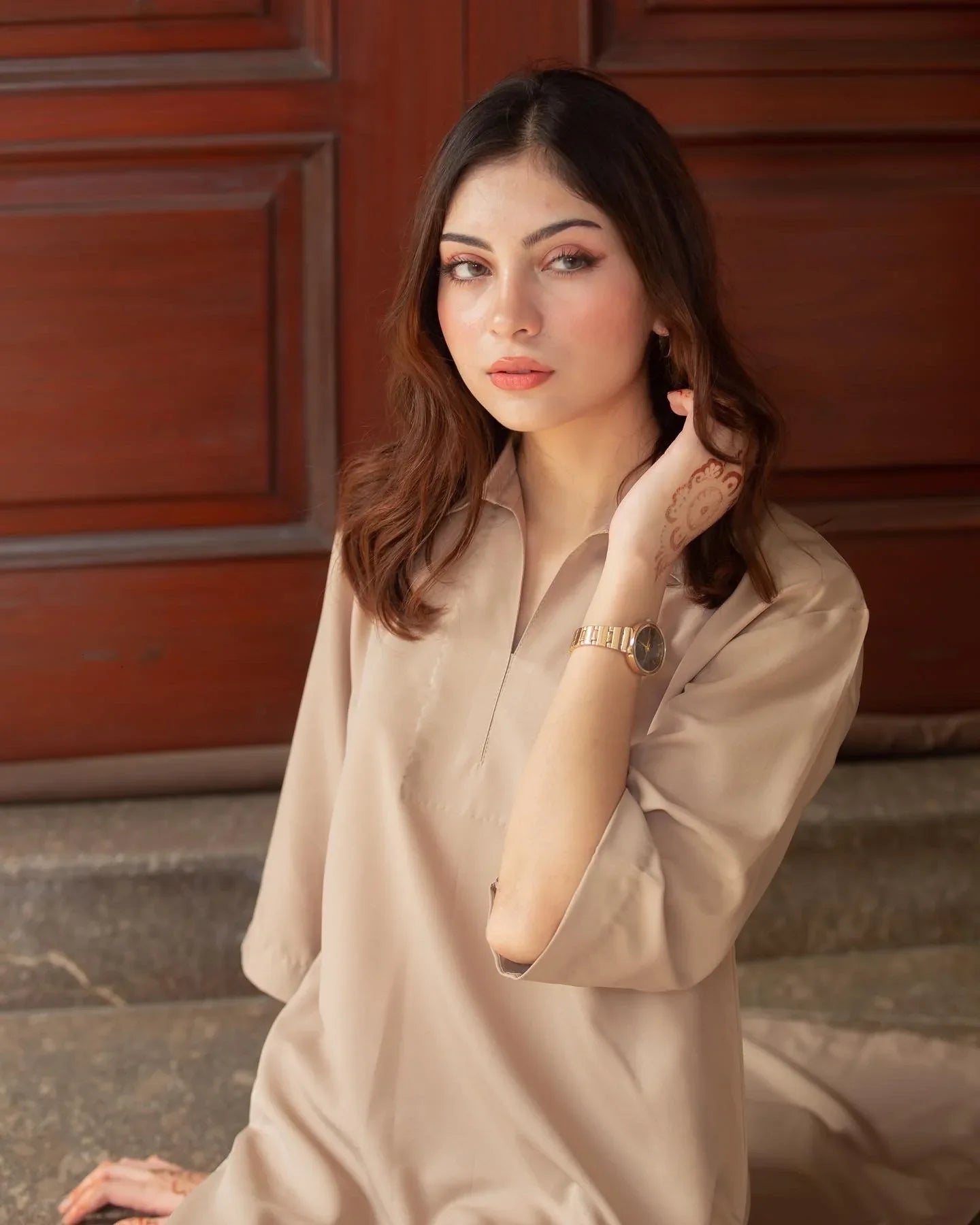 A woman in a Phone Dress sitting in front of large wooden doors with a thoughtful expression. 
