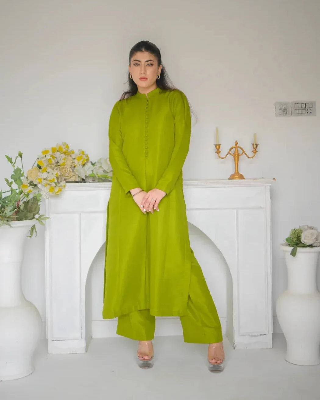 Woman in a green dress standing in a room with white walls and decorative elements. it is a simple dress for mehndi.