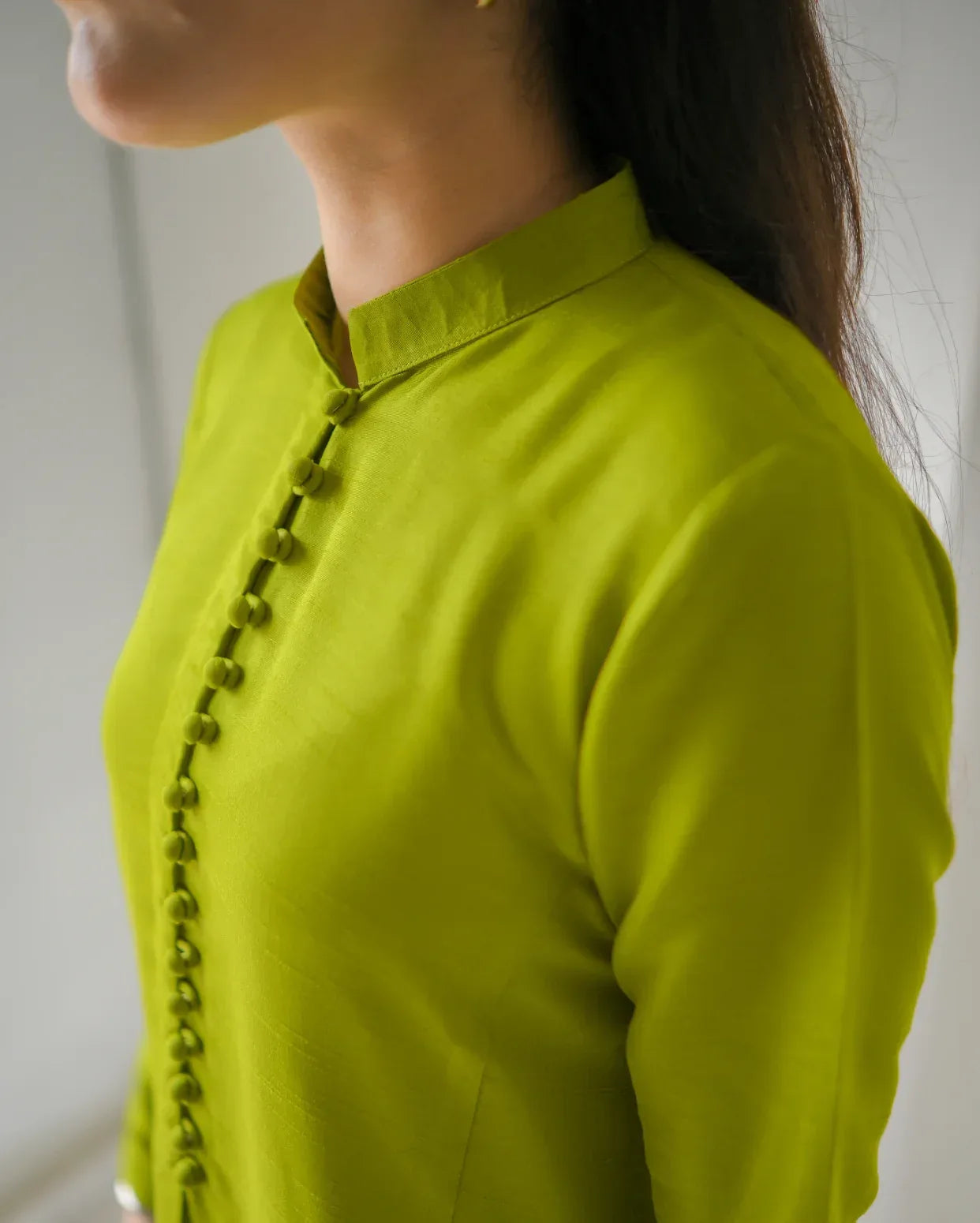 Close-up of a person wearing a bright green top with button details on a plain background