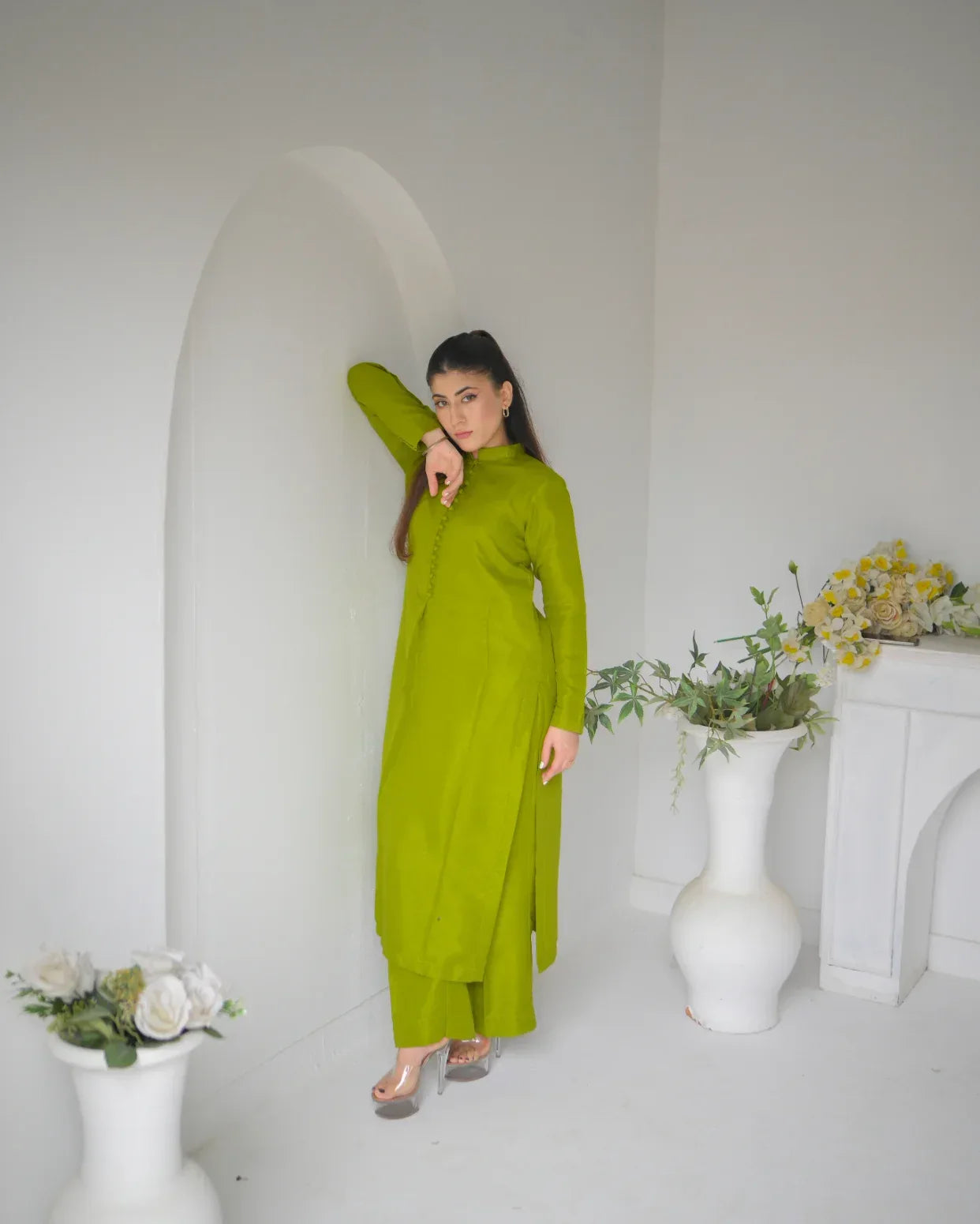 Woman in a green outfit standing in a minimalistic room with white walls and decor. This Dress is wearable in mehndi.
