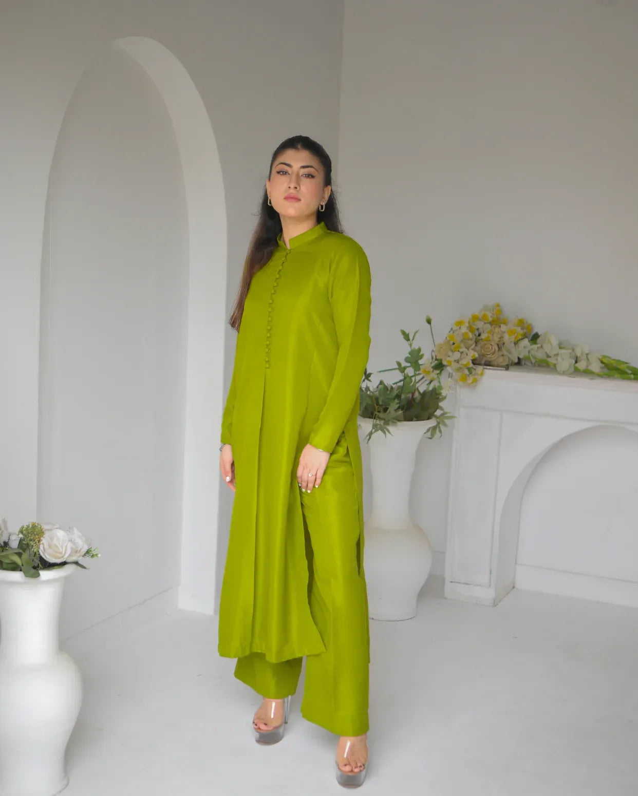 Woman in a green mehndi dress standing in a white room with decorative elements.