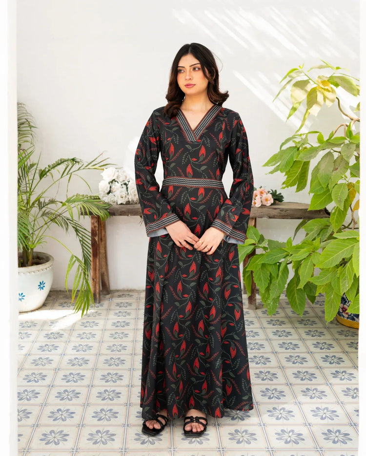Woman wearing a black printed dress standing in a room with plants and a tiled floor.