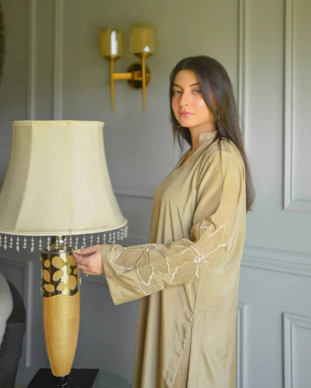 A woman in a beige traditional outfit with embroidery details on sleeves.