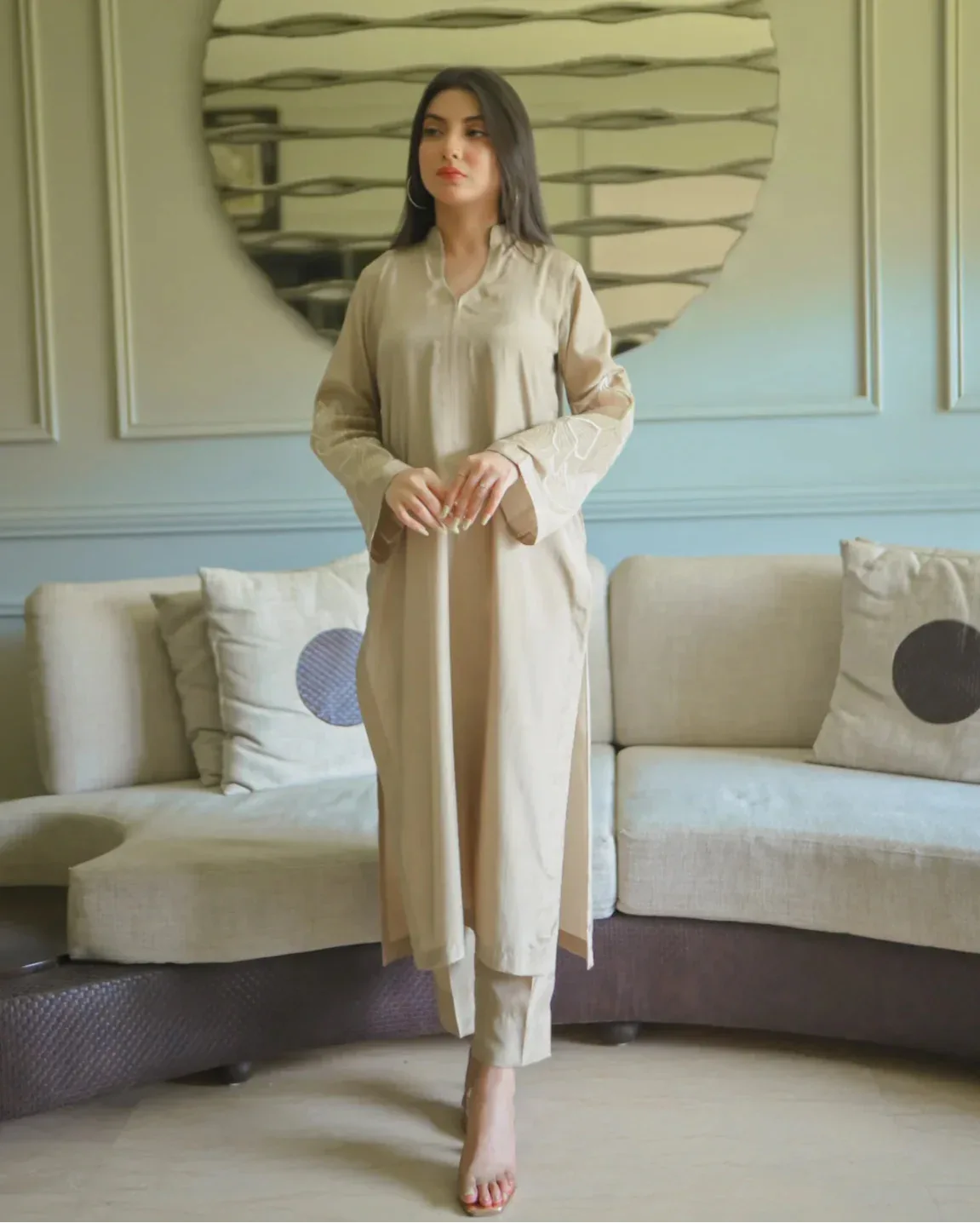 A woman in a beige traditional outfit with embroidery details on sleeves.