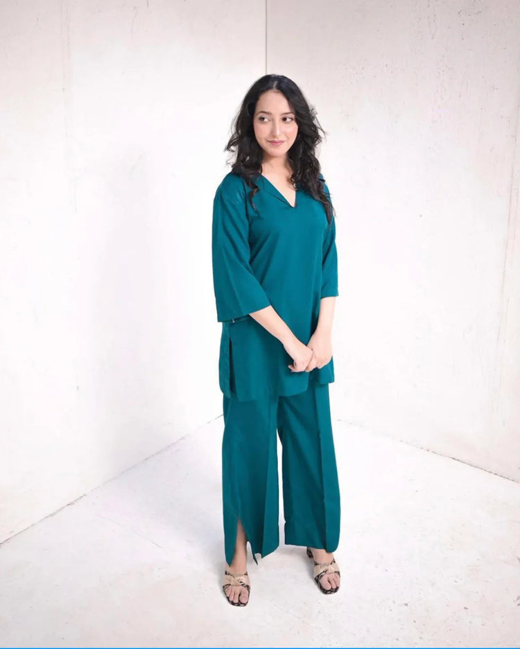 Woman wearing a teal green outfit standing against a white background