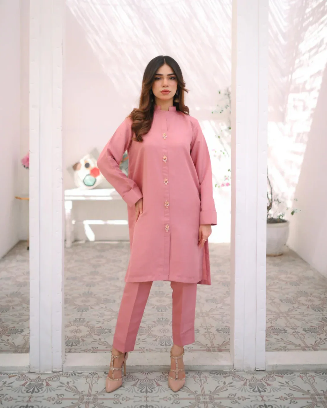 A woman wearing a pink two-piece indian rawsilk dress consisting of a shirt and trousers.