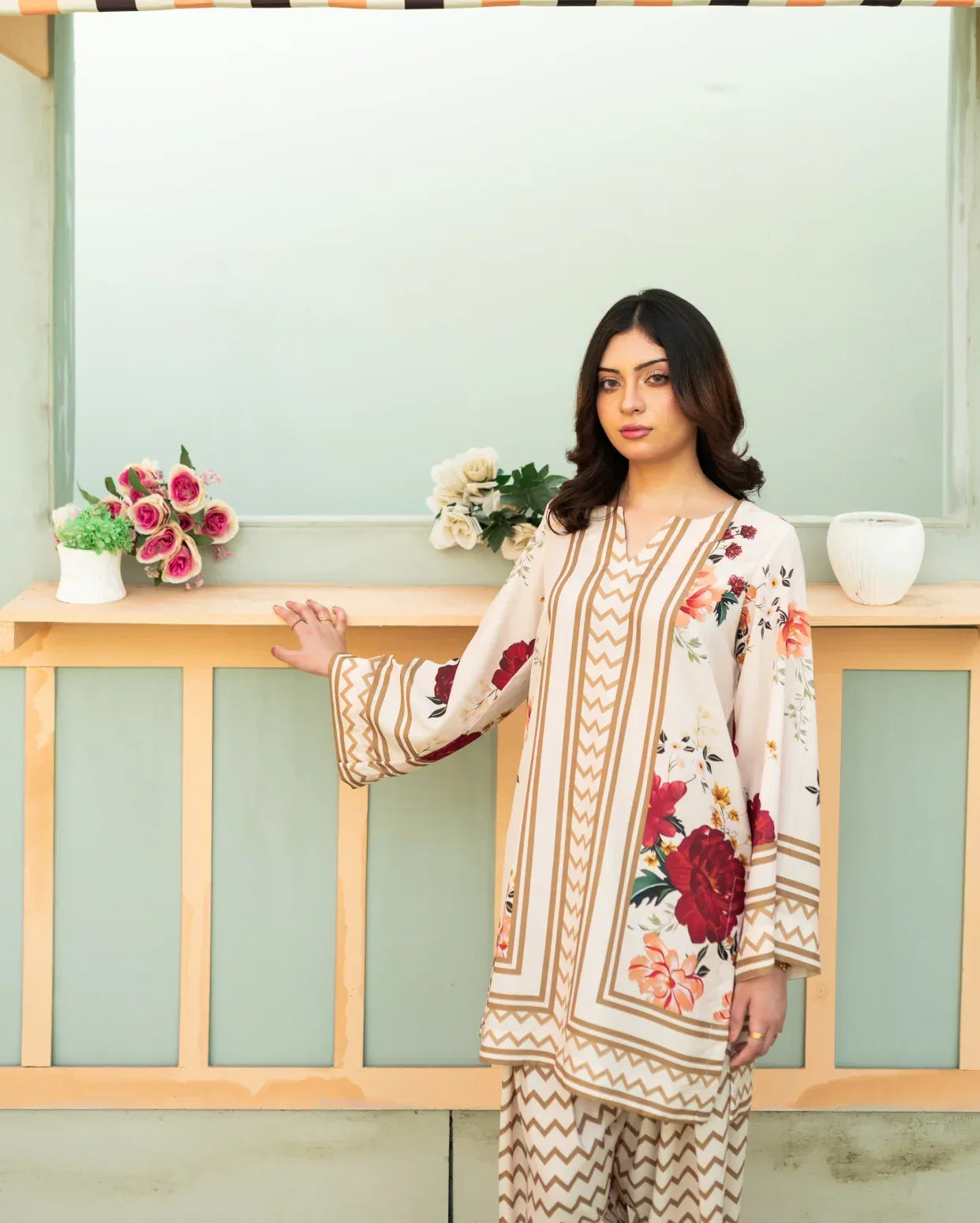 Woman wearing a floral outfit standing indoors with decorative elements.
