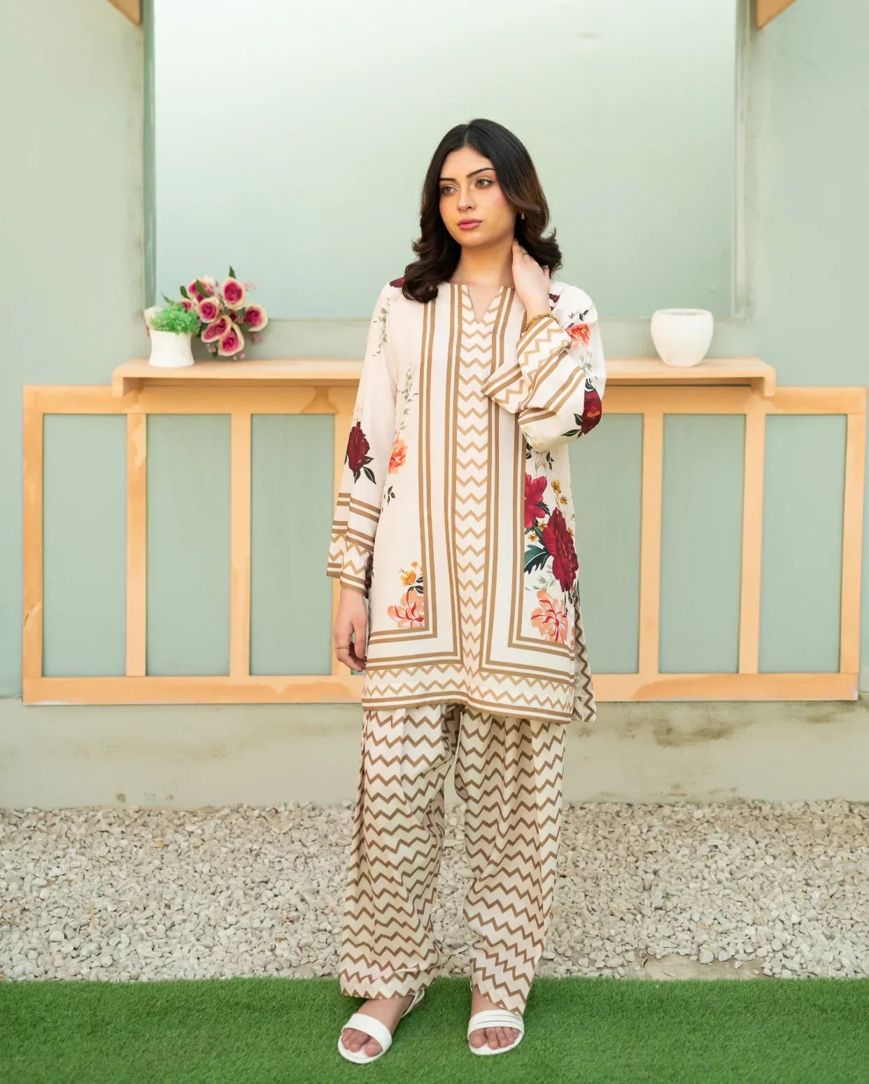 Woman wearing a floral two piece outfit standing in front of a light green wall with wooden shelves.