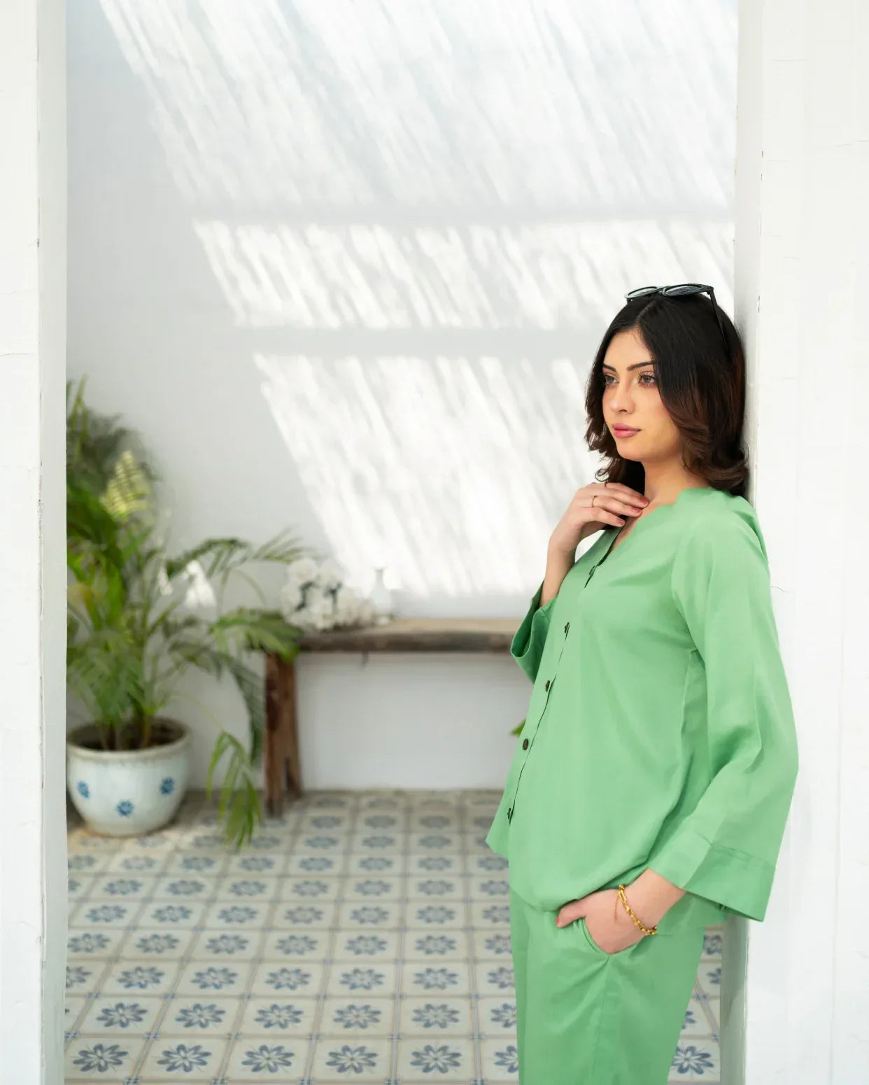 Woman in a green suit standing in a room with plants and a tiled floor.