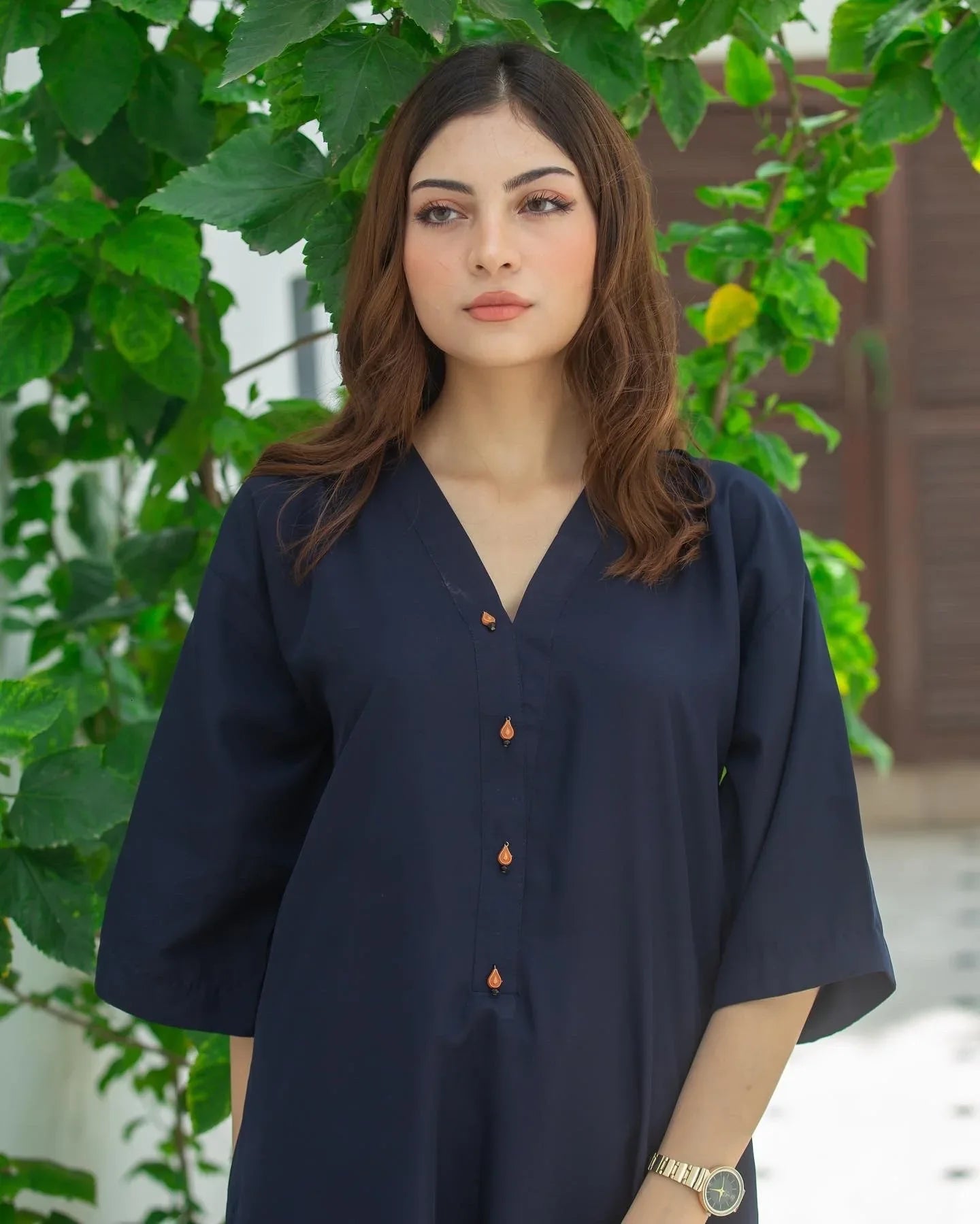 Woman in a navy blue dress standing outdoors with greenery in the background