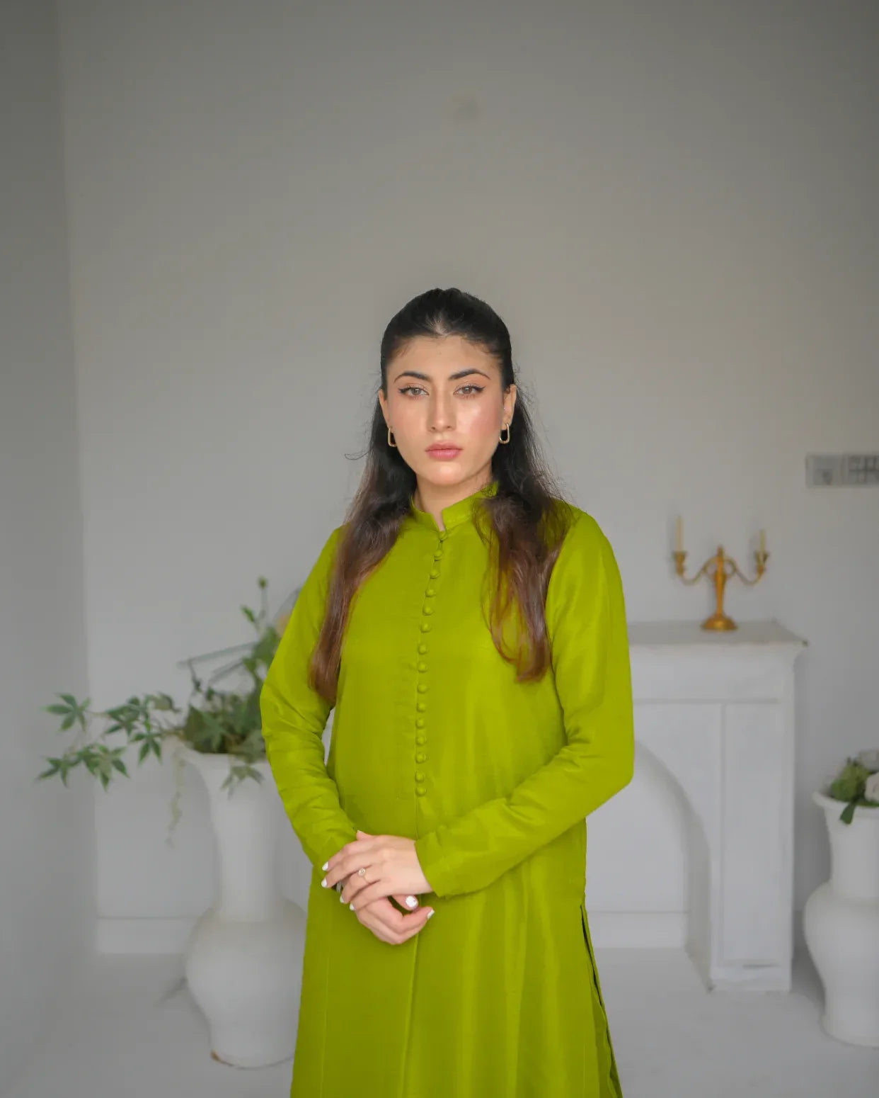 Woman in a simple mehndi dress standing in a white room with decorative elements.