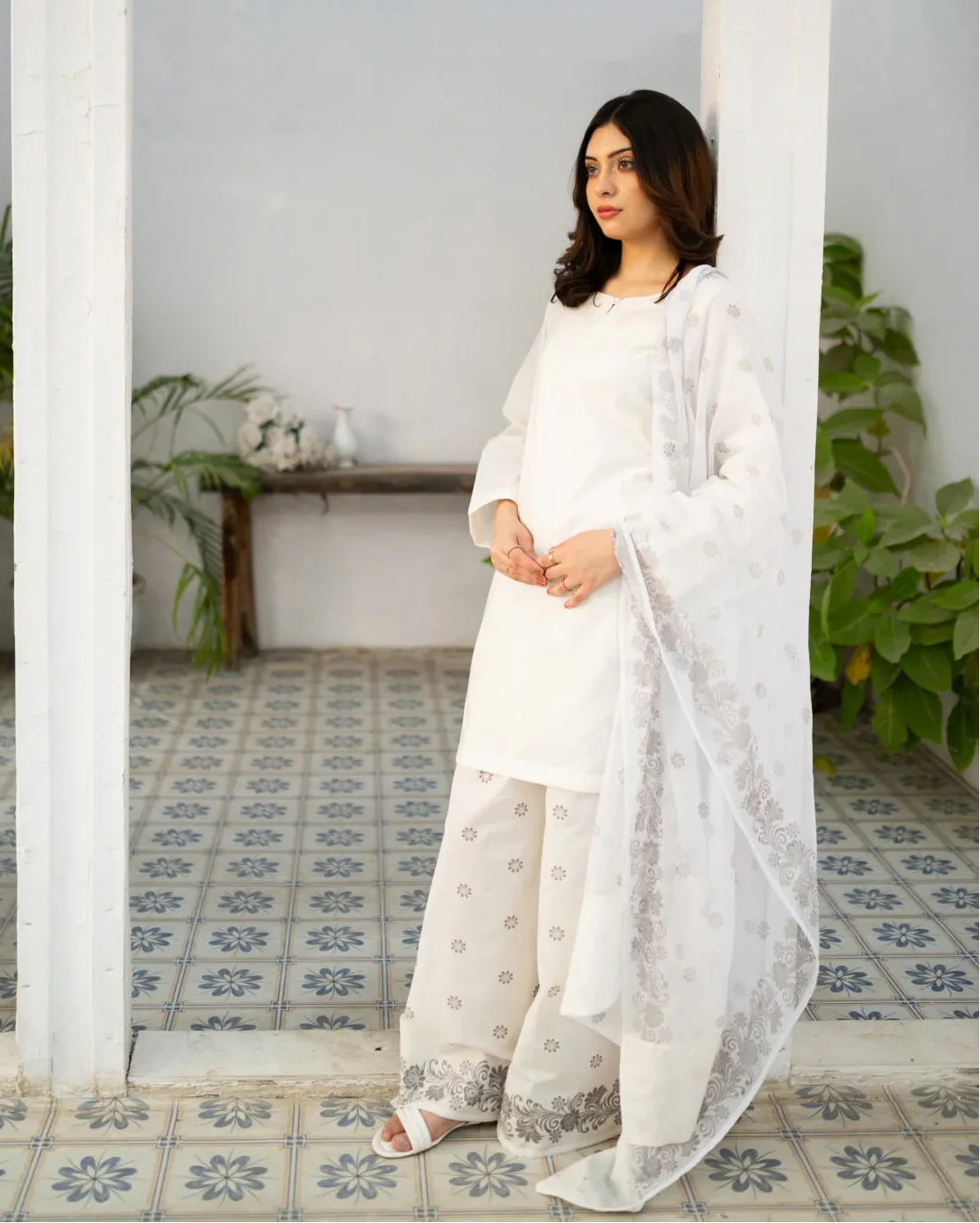 Woman in a white dress, a traditionally kurta set standing in a room with decorative tiles and plants.