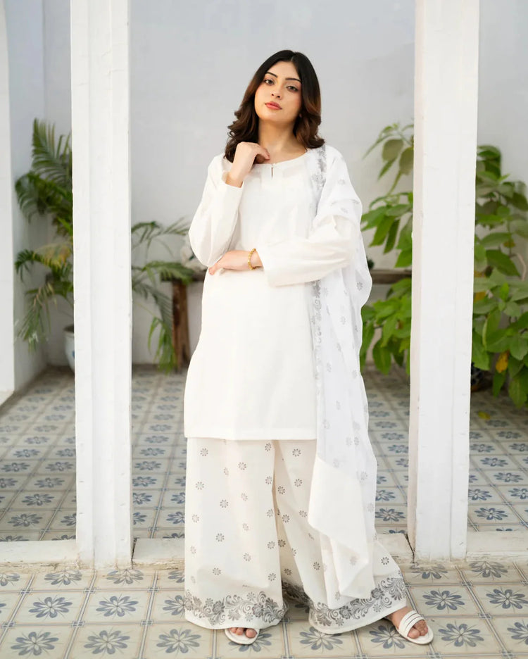 Woman in a white traditional kurta set standing in a decorative interior setting with plants.