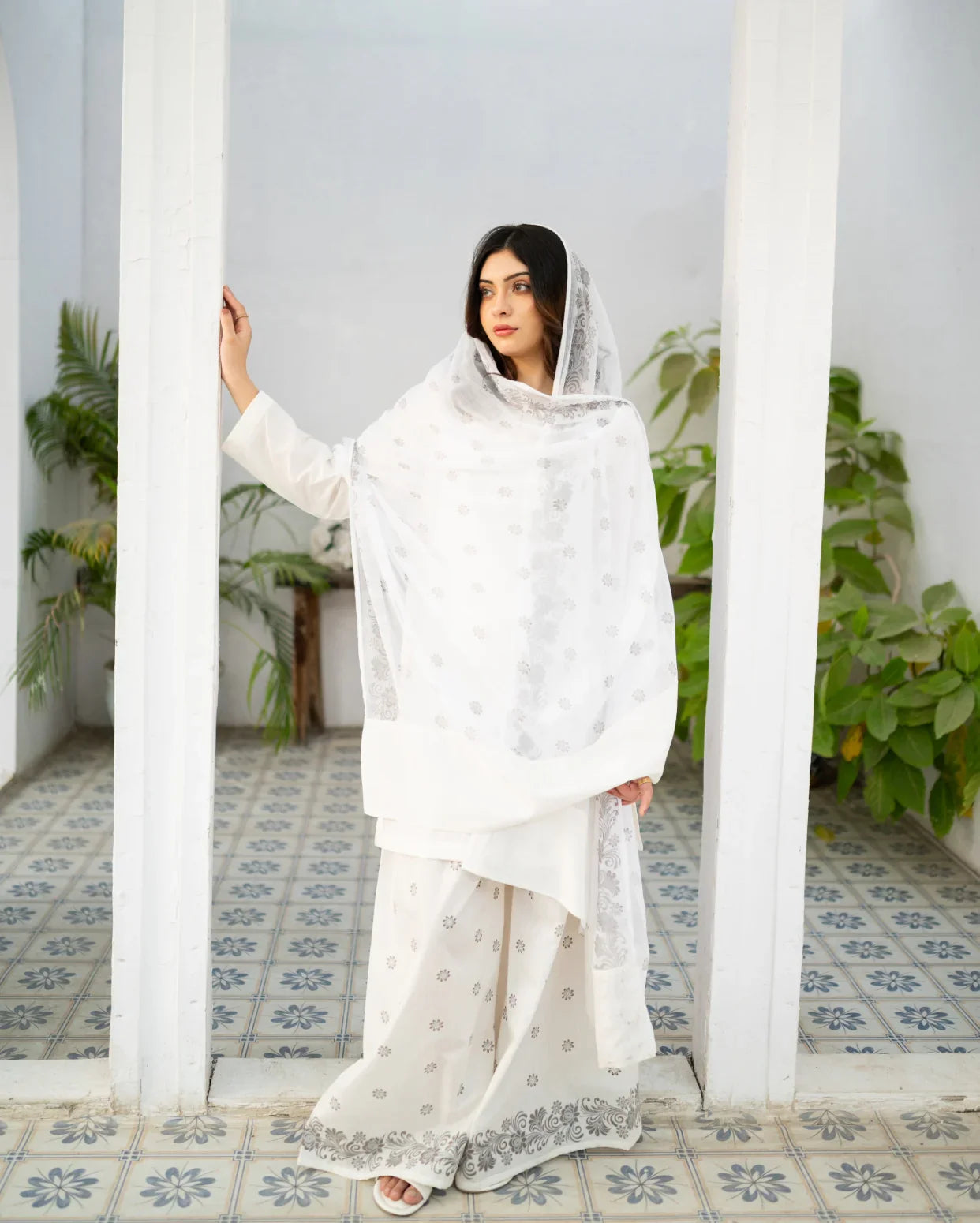 Woman in a white dress, a traditional kurta set standing in a room with plants and patterned floor.