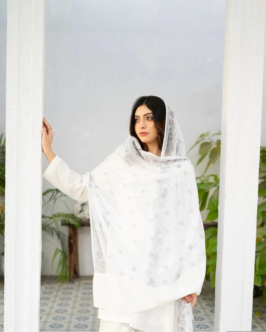 Woman in a white traditional kurta set standing between white pillars with greenery in the background